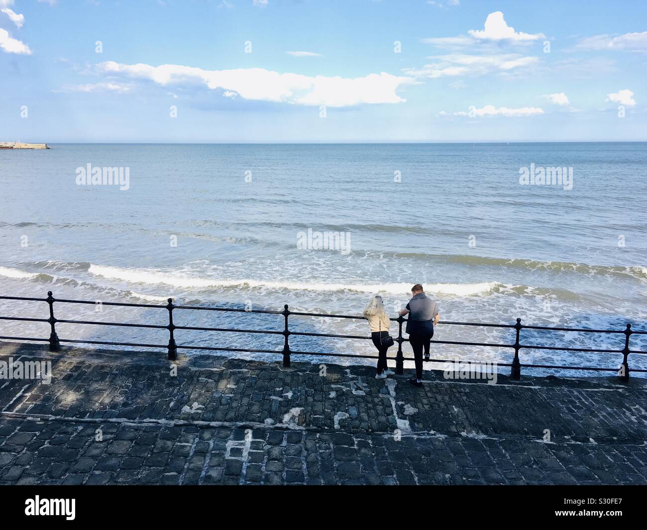 Couple looking over railings at Scarborough, Yorkshire coastline from the South Bay - Smartphone Captured Stock Image