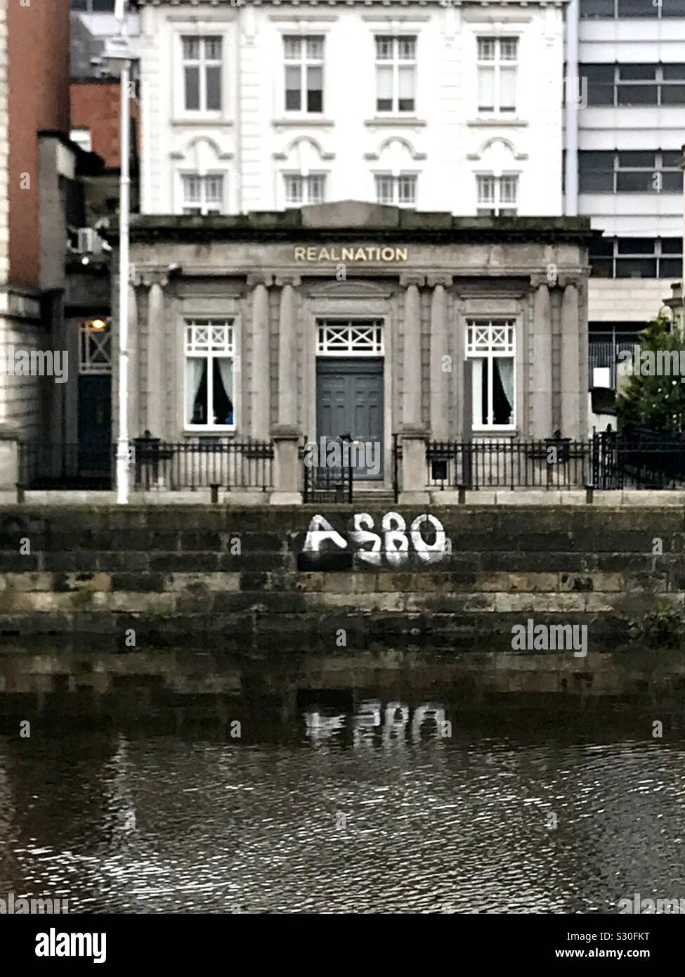 An old bank building by the River Liffey in Dublin, Ireland. ASBO written as graffiti on a wall nearby. (Anti-social behaviour order) - Smartphone Captured Stock Image
