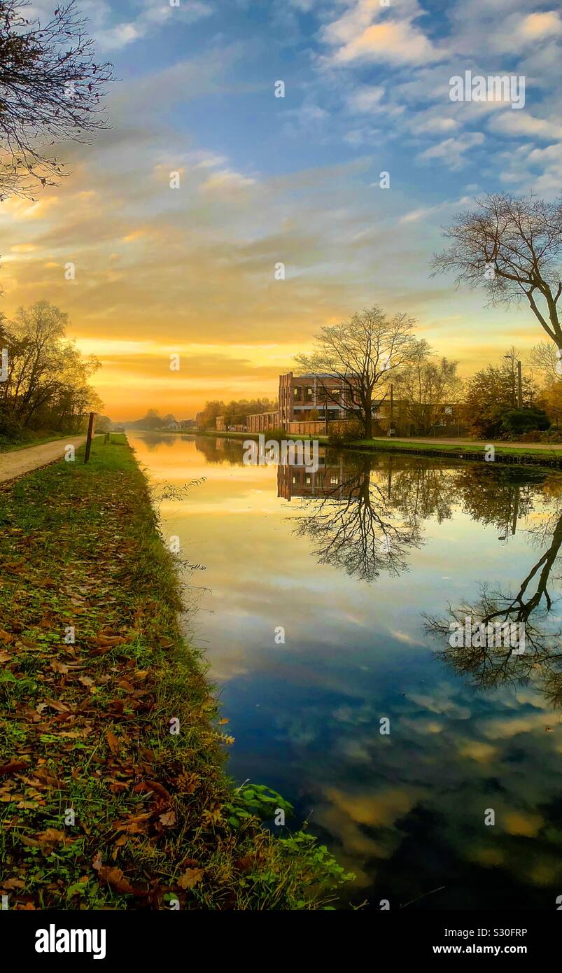 Dramatic and colorful sunrise or sunset over a Countryside river or canal landscape with the sky and clouds reflected in the water - Smartphone Captured Stock Image
