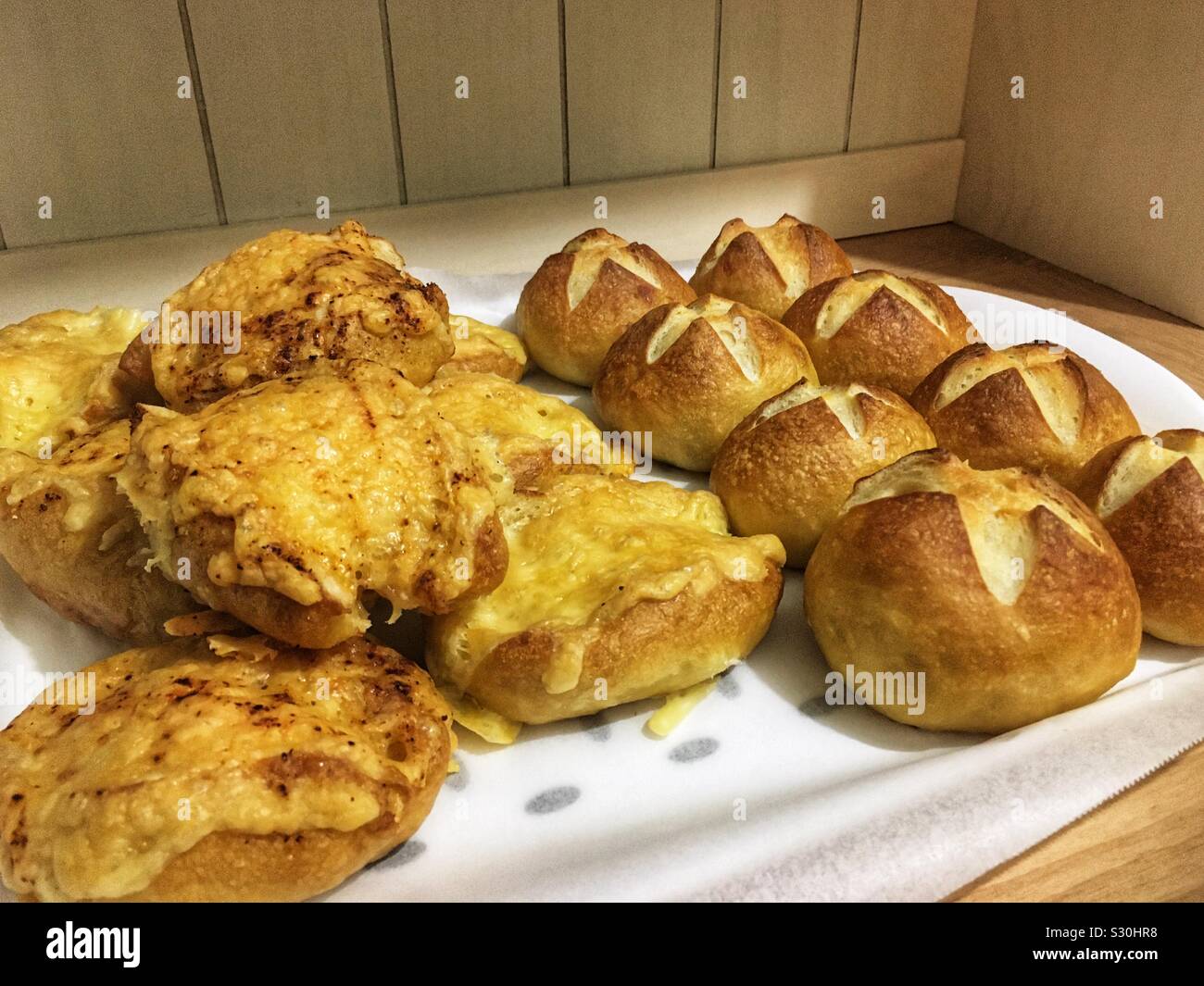 A tray of home made German pretzel buns and cheese pretzel buns (Laugenbrötchen) on a kitchen counter. Stock Photo