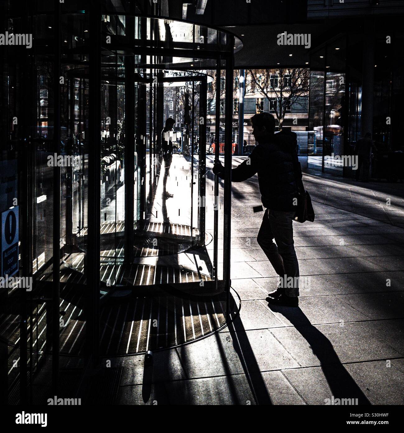 A man in silhouette enters a revolving door Stock Photo