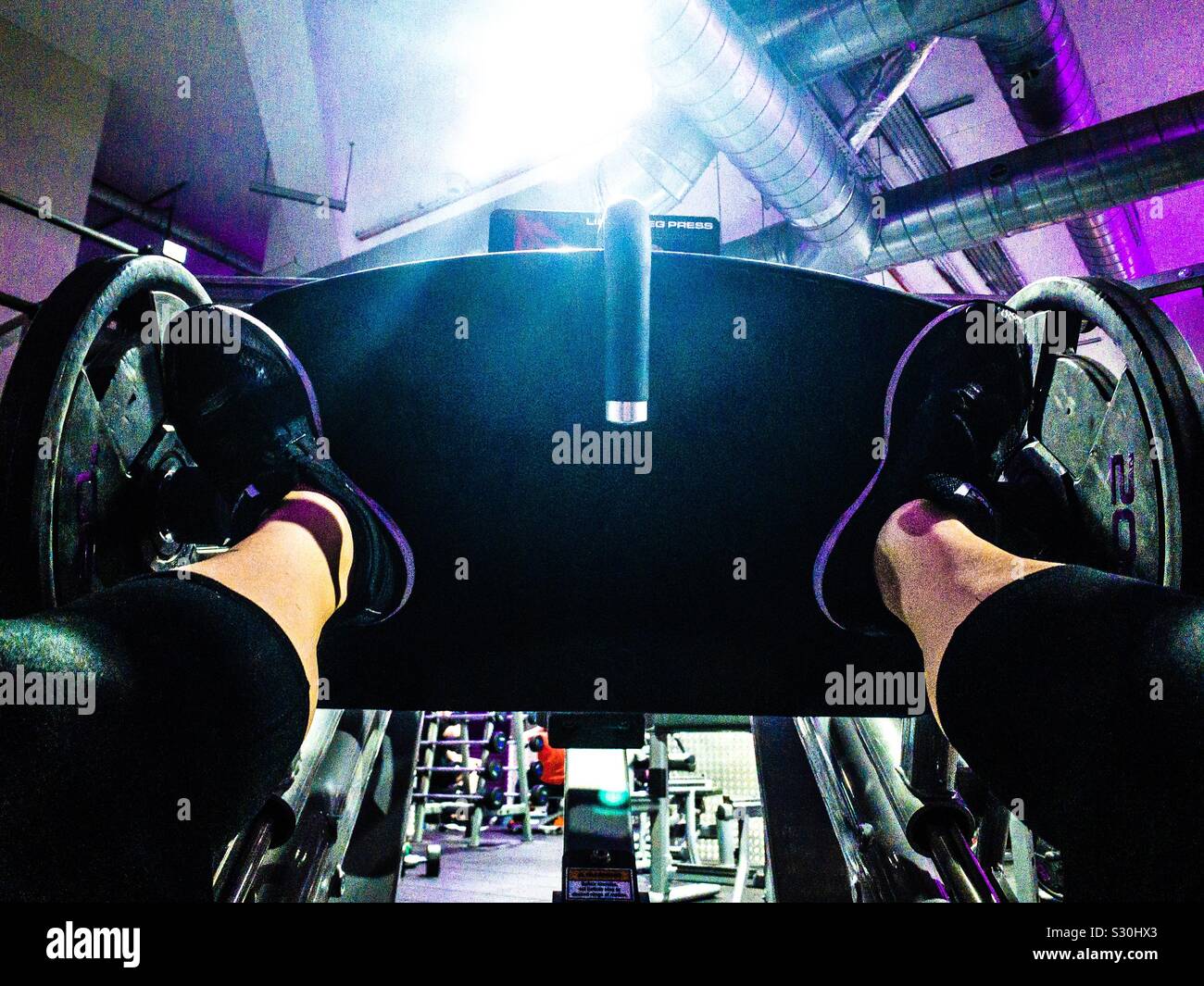 A woman uses a leg press in a gym - Smartphone Captured Stock Image