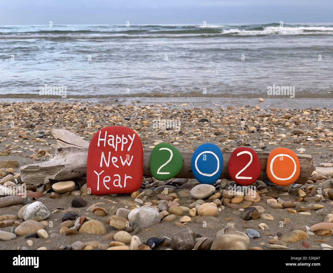 Happy New Year message with a creative composition of colored and carved stones with beach background - Smartphone Captured Stock Image