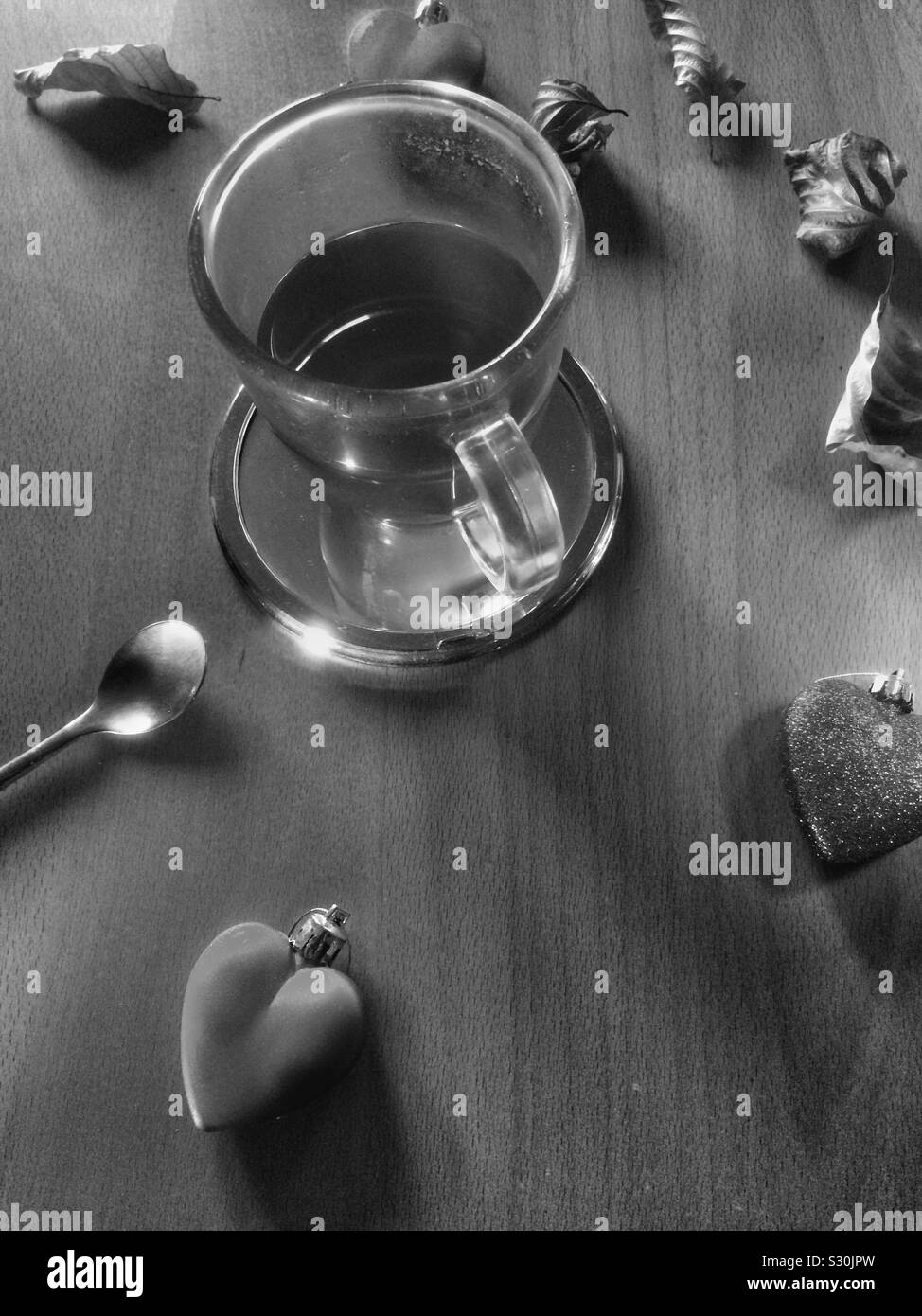 Cup of tea made of transparent glass with decorative hearts around and dried Autumn leaves. Stock Photo