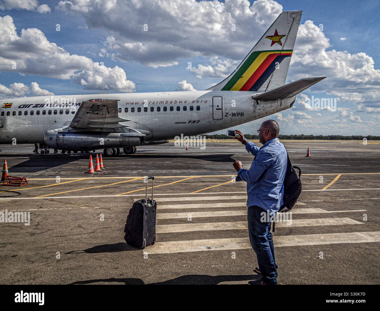 A man takes a photo of Air Zimbabwe Boeing 737-200 registration Z-WPB at Victoria Falls airport, Zimbabwe. March 2015. Stock Photo