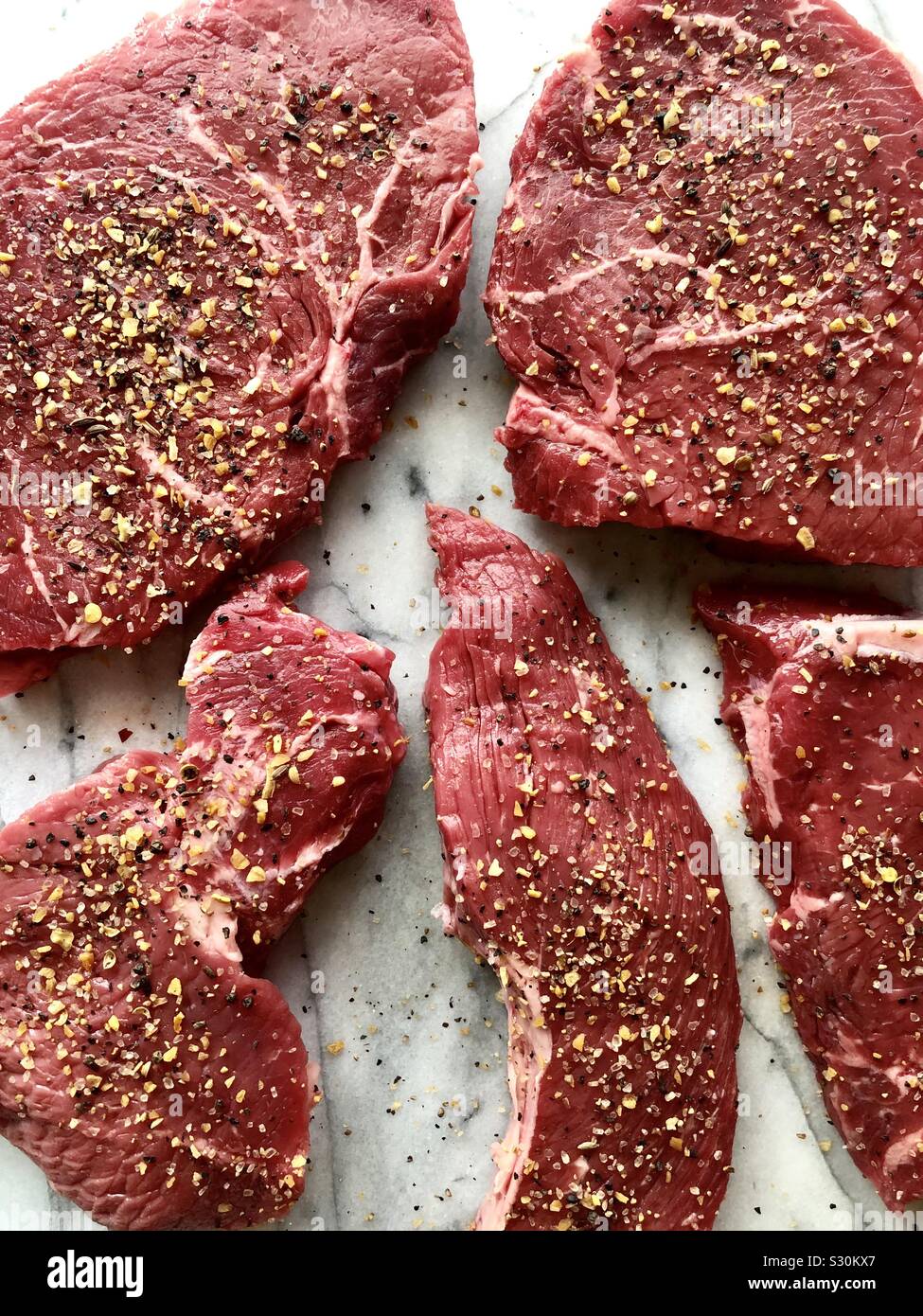 Uncooked, seasoned sirloin steaks on a white marble cutting board - Smartphone Captured Stock Image