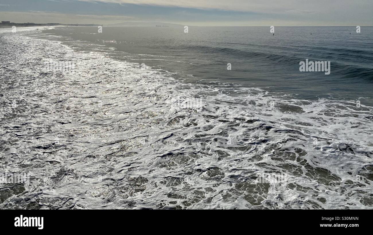 Sea foam near the shore on Pacific Coast in California, with mountains and ships on the horizon - Smartphone Captured Stock Image