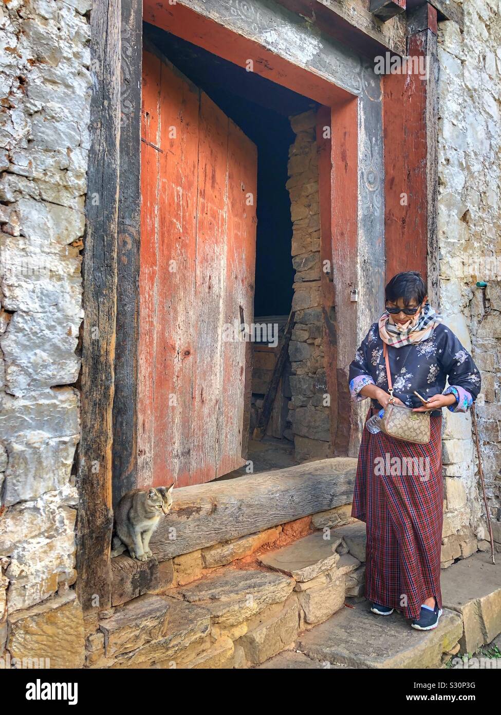 Bhutanese woman and cat in front of an old building. - Smartphone Captured Stock Image