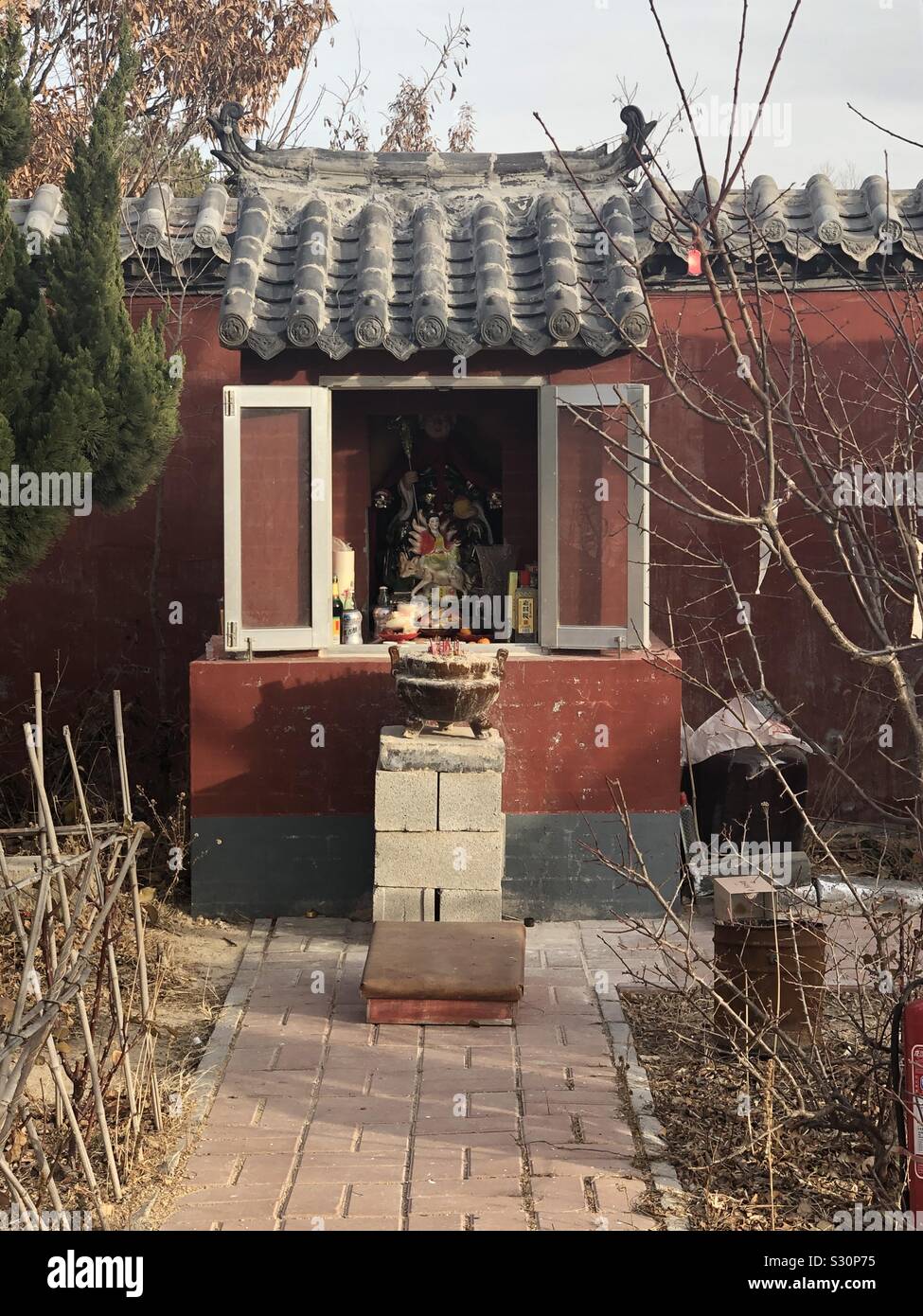 A shrine inside a temple in China, Shandong province showing flower beds,tree, shrubs, fire extinguisher. Stock Photo