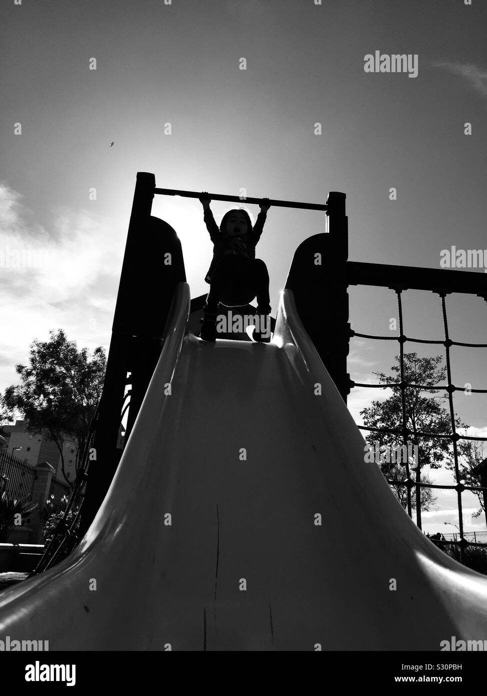 Shadows of a child Swinging at the top of the slide with a bright sky. Stock Photo