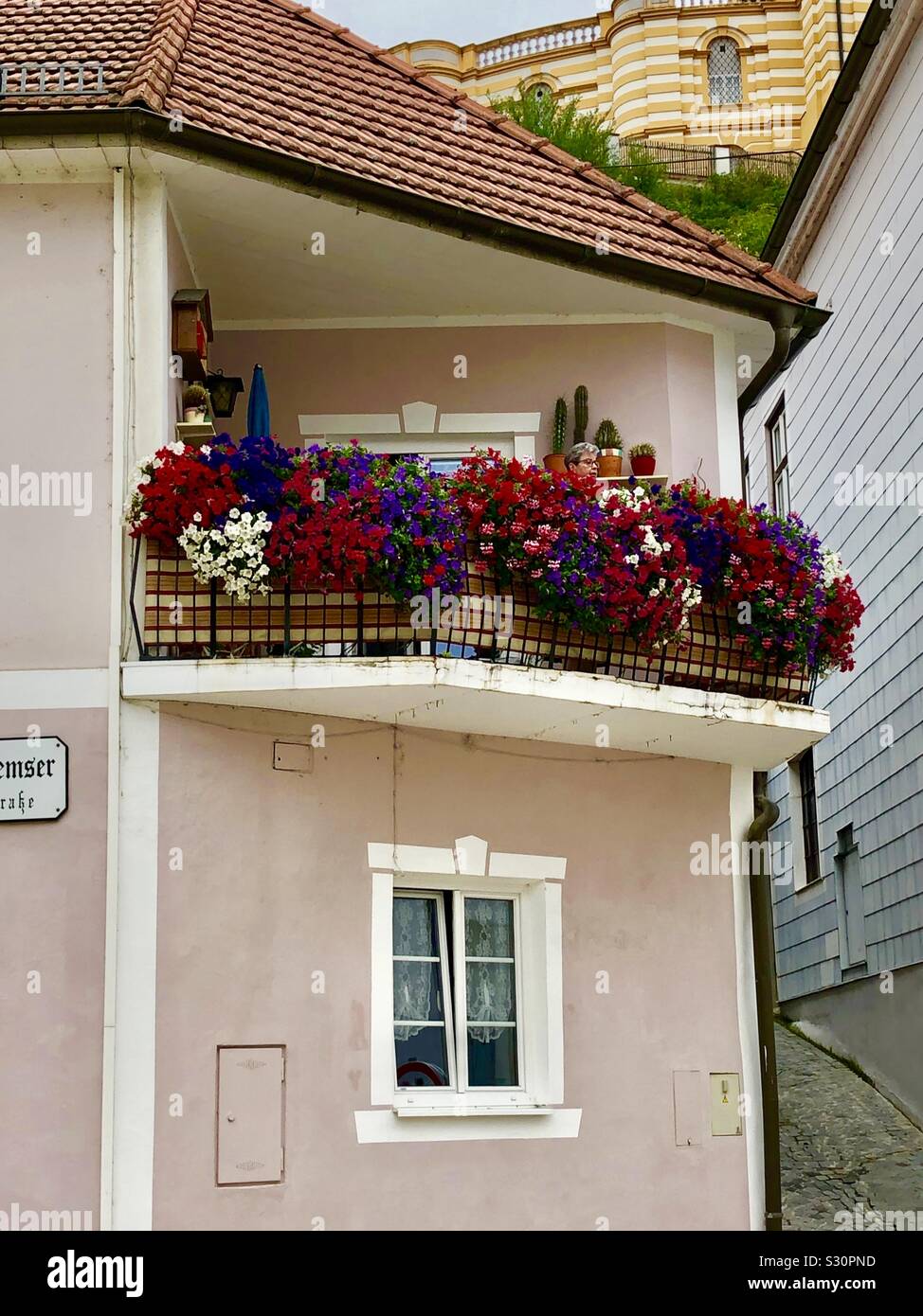 Colorful housing and garden in Melk, Austria showing an upstairs patio and garden with a woman tending to her plants. Stock Photo