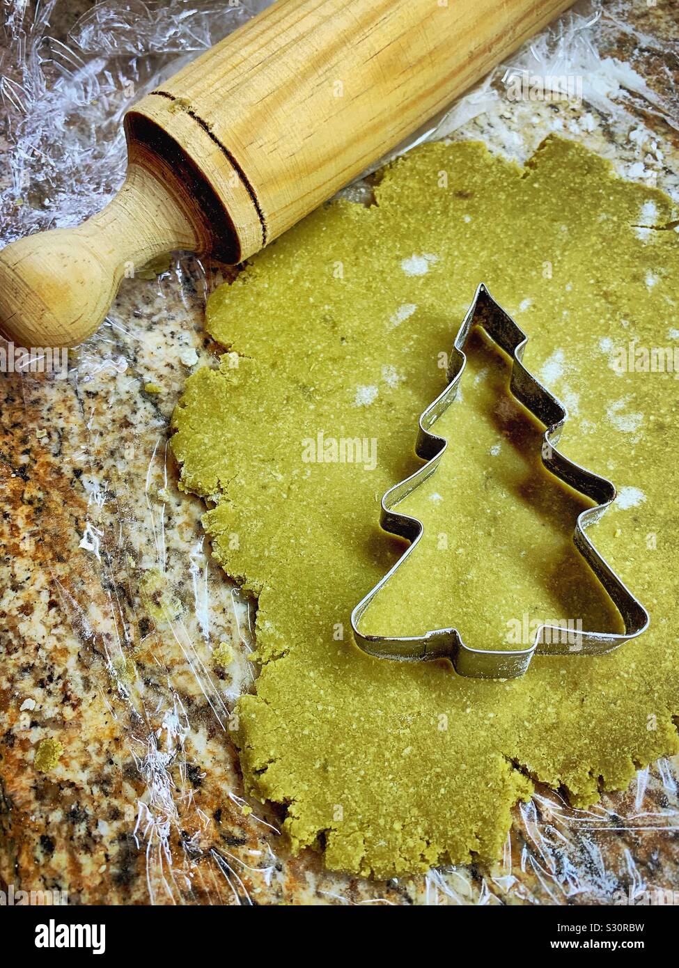 Green matcha cookie dough is rolled out and ready to be cut into Christmas tree shapes with a cookie cutter. Stock Photo