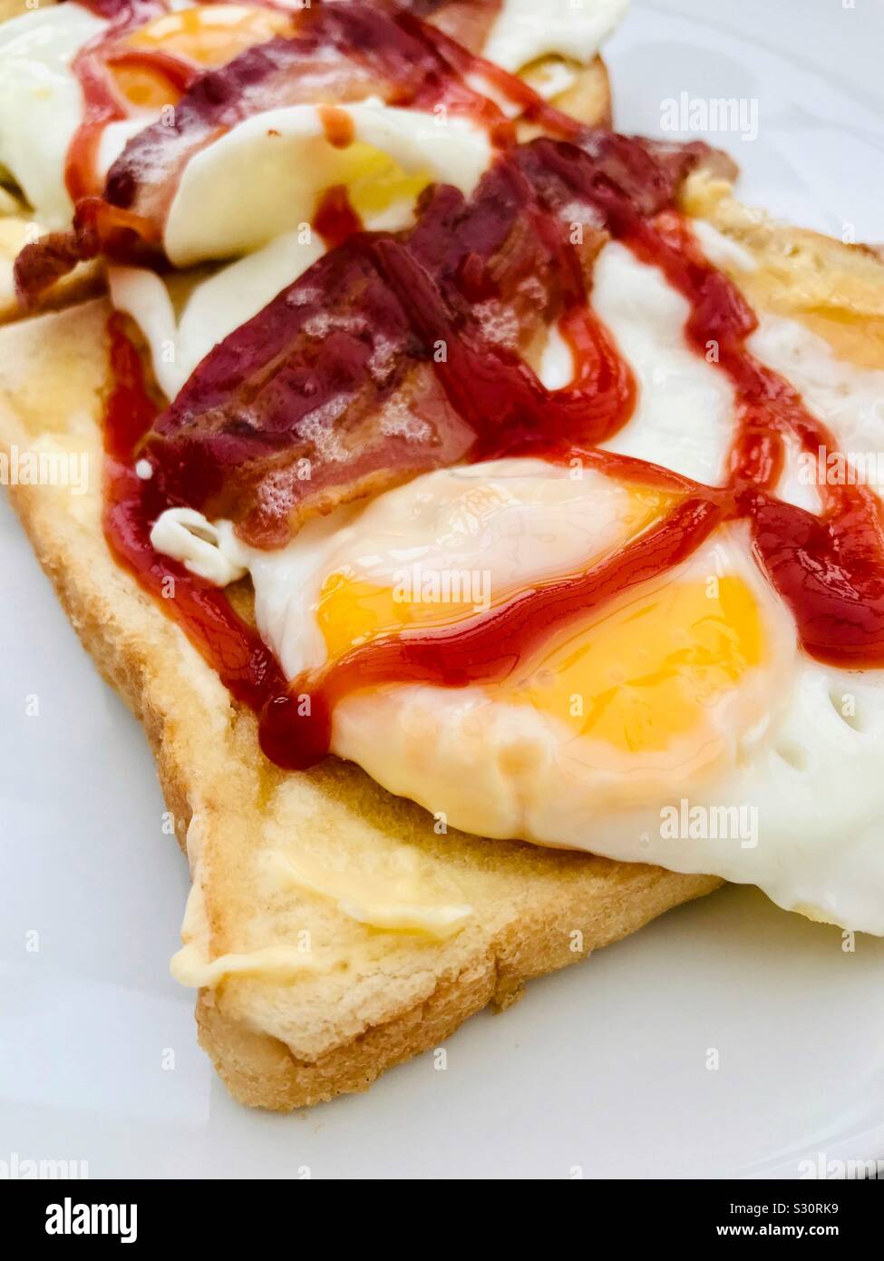 Breakfast fried egg, with streaky bacon on white toast with tomato ketchup Stock Photo Alamy