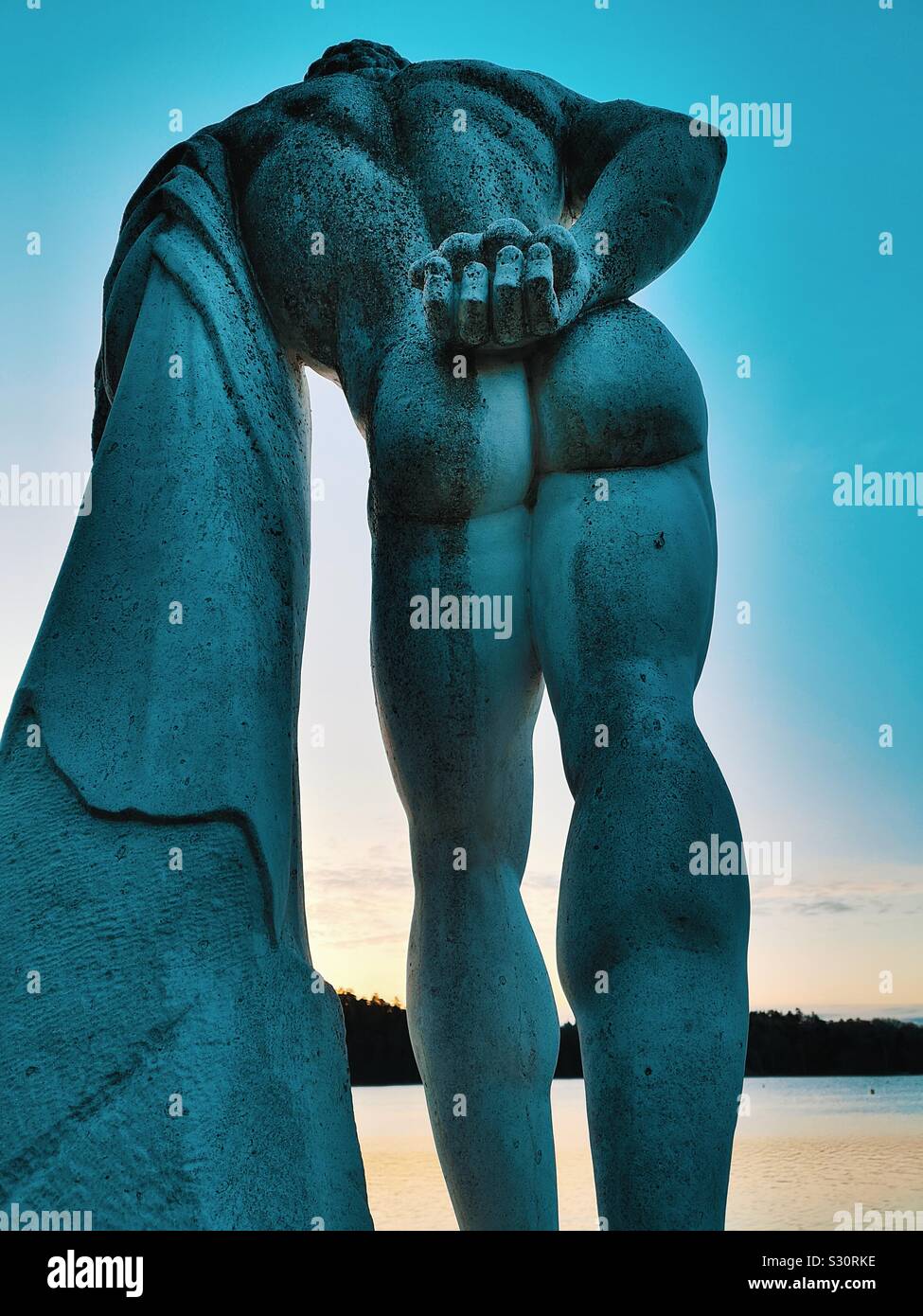 Rear view of naked male sculpture statue by lake at dawn, Sweden Stock Photo