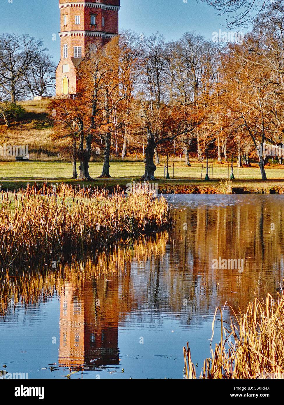 Gothic tower reflected in river, Drottningholm Palace Gardens, Drottningholm, Stockholm County, Sweden. Drottningholm is the private residence of the Swedish Royal family. Gothic tower was built 1792. Stock Photo