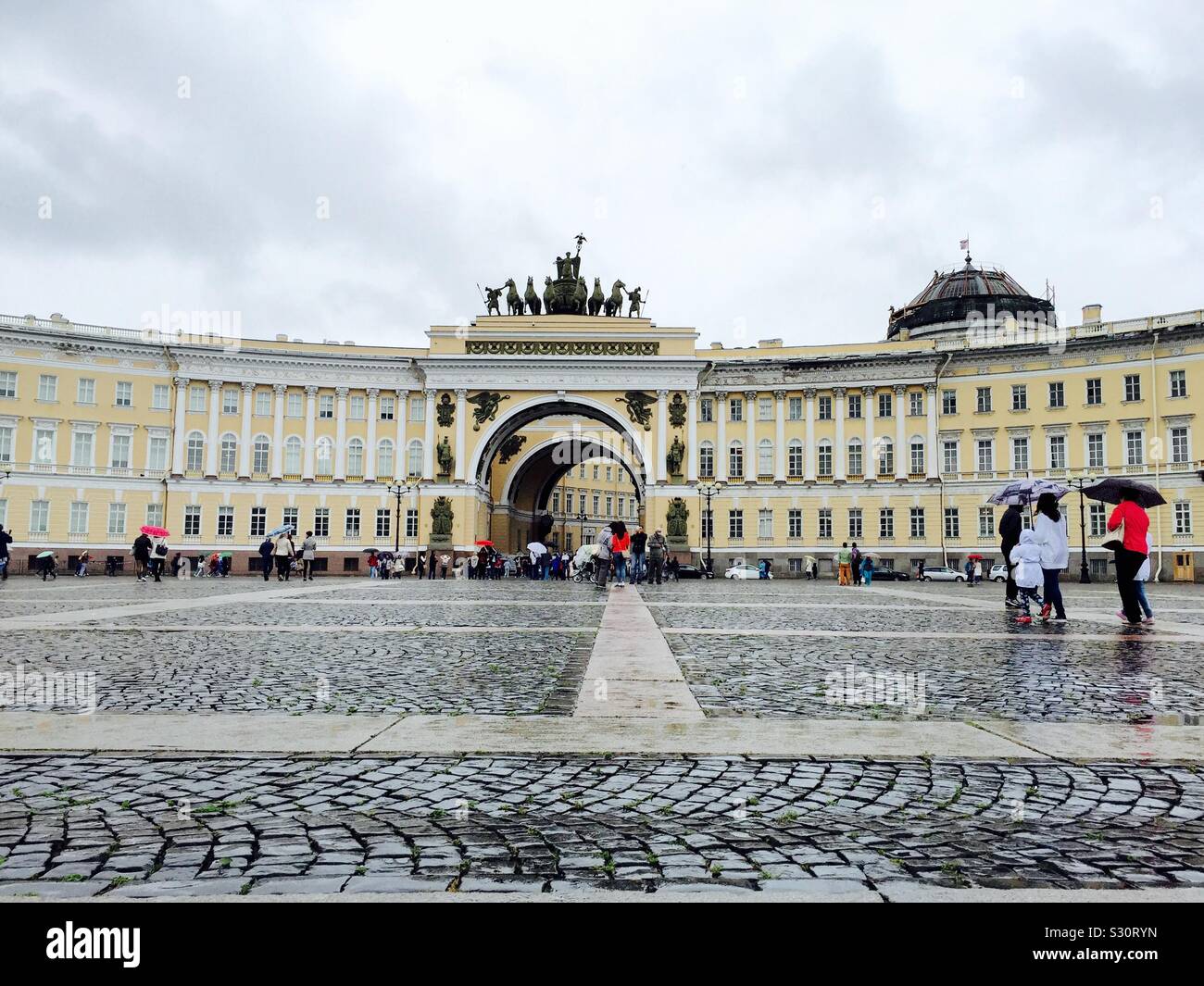 Low perspective view across St. Petersburg’s cobbled stoned Palace Square to the General Staff Building on rainy day. Famous Russian architectural landmark, General Staff Building. Stock Photo