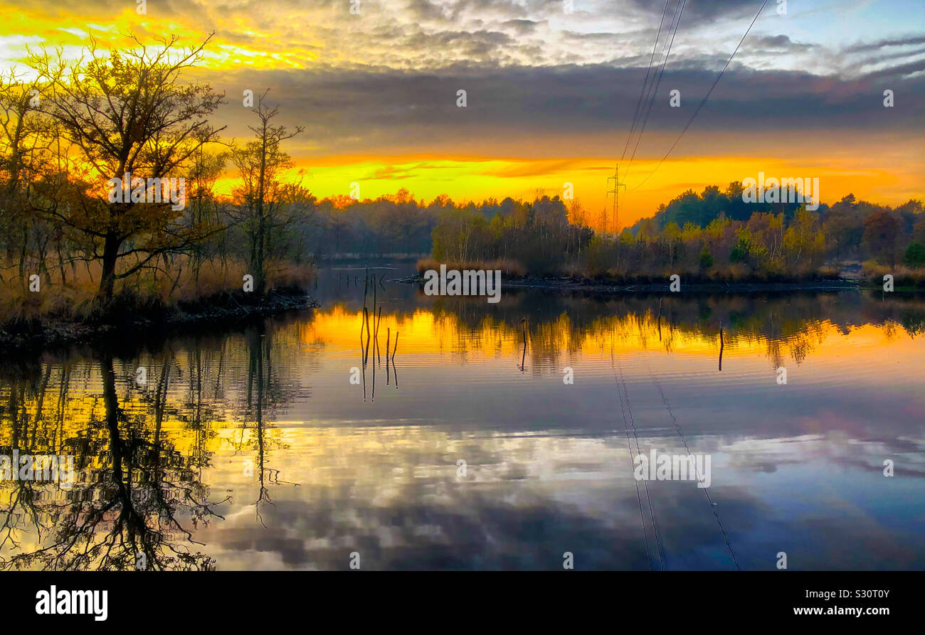 Colorful and dramatic sunrise or sunset sky over a forest lake, with reflections in the water - Smartphone Captured Stock Image