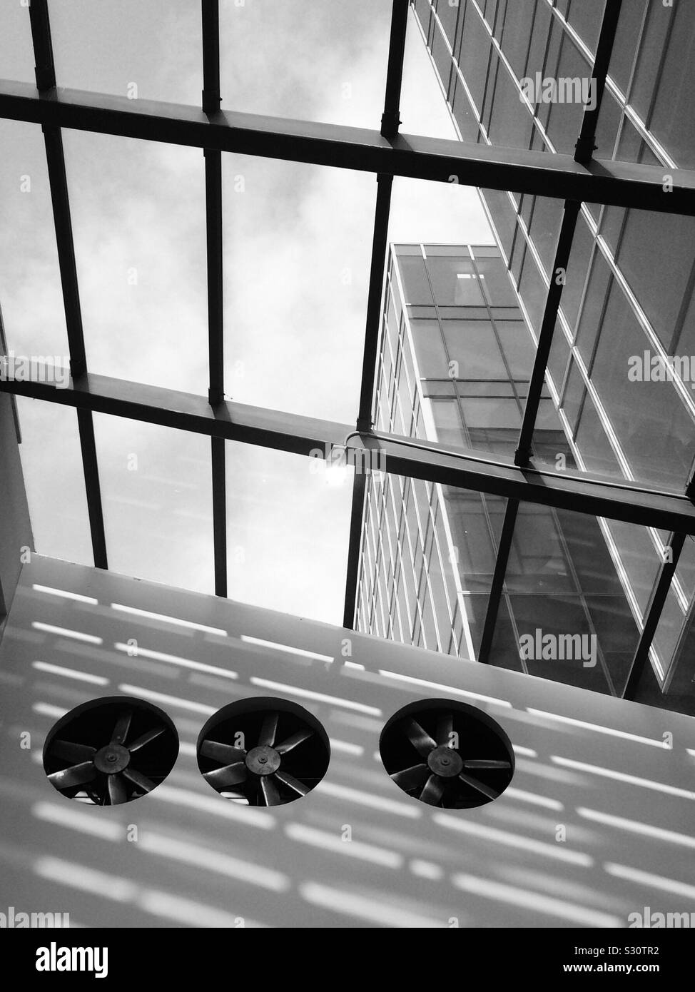 Dramatic interior view with industrial fans and skylight and office building as seen through glass ceiling Stock Photo