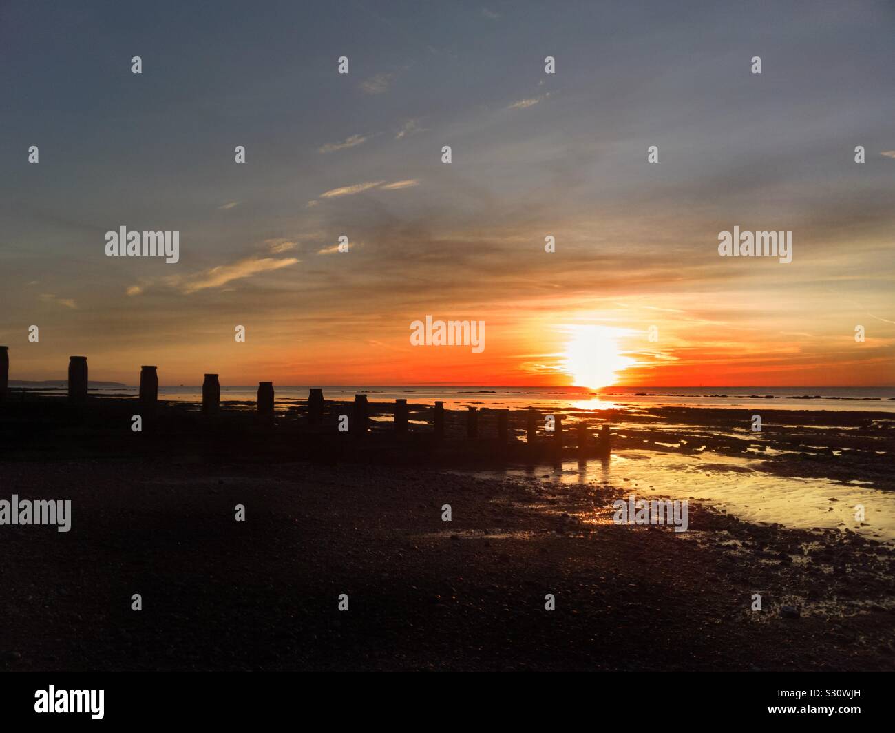 Sunrise on Eastbourne beach in the UK, at low tide with the rock pools reflecting the sun Stock Photo
