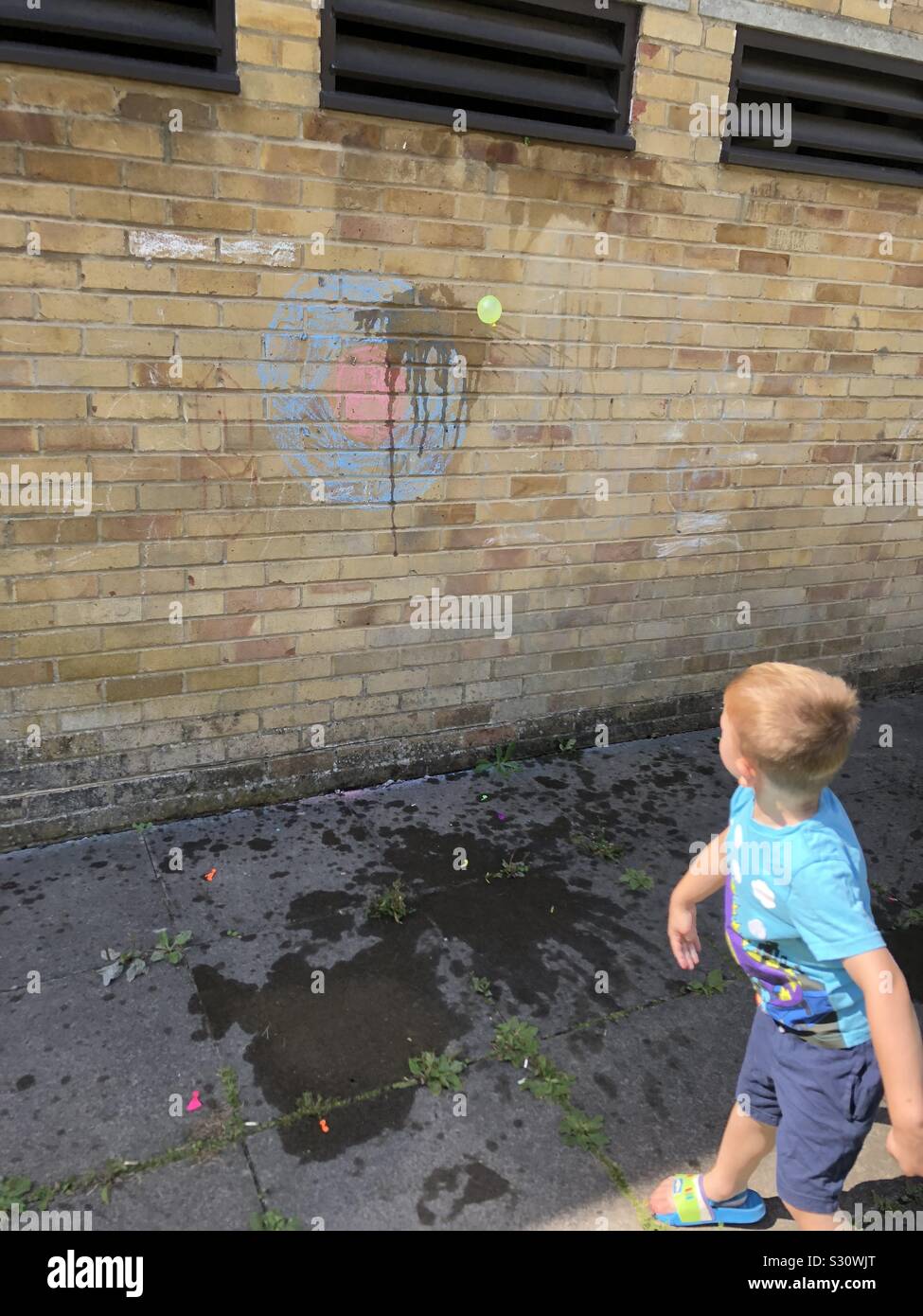 Boy throwing water ballon and chalk drawn target on wall Stock Photo