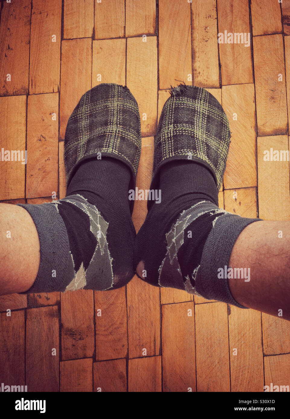 Top view on male legs wearing old worm socks and slippers standing on old parquetry Stock Photo