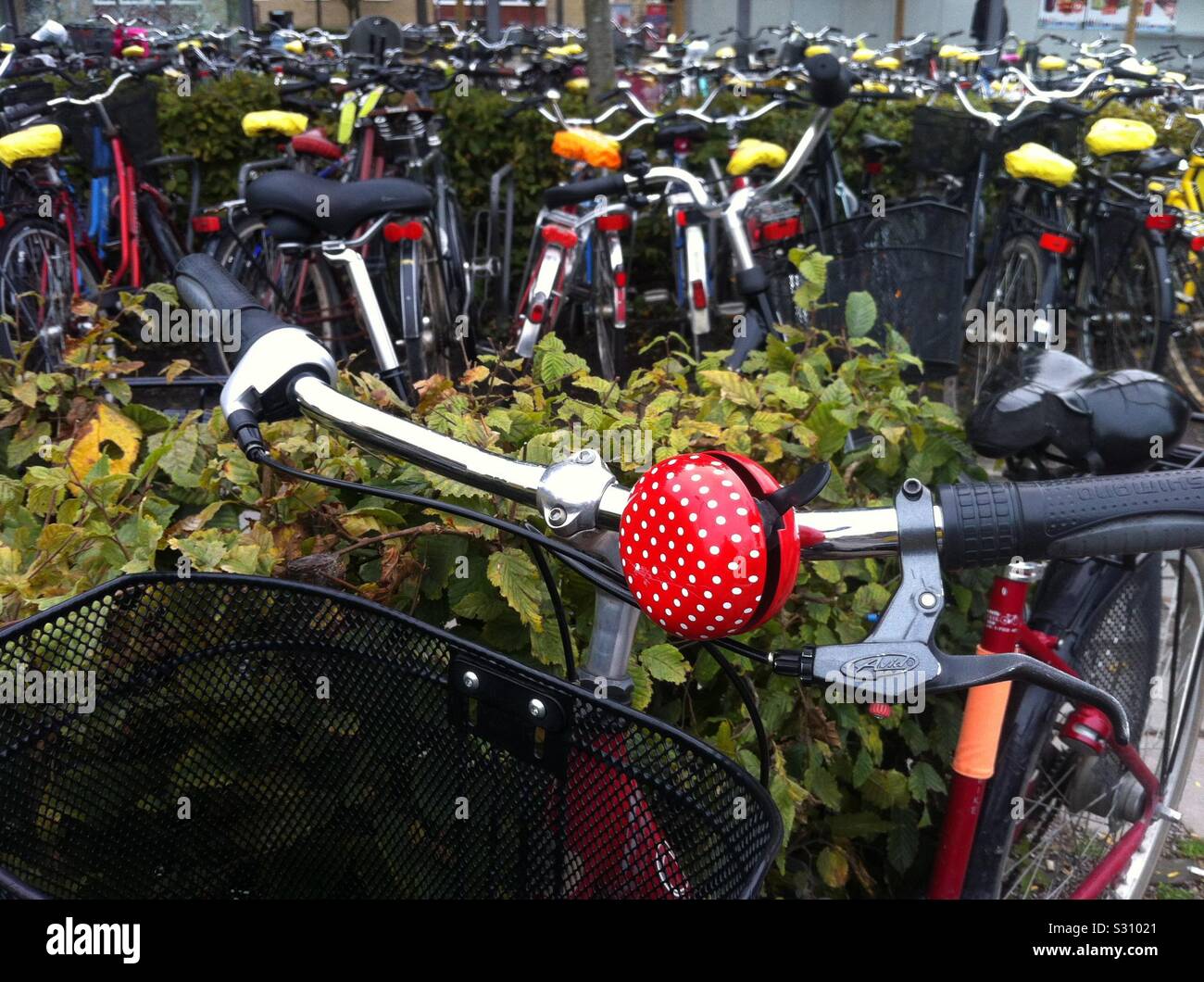 Closeup shot of a red and white spotted bicycle bell and parked bikes in background. Uppsala city train station parking soon to host a huge indoors new parking site. Sweden Stock Photo