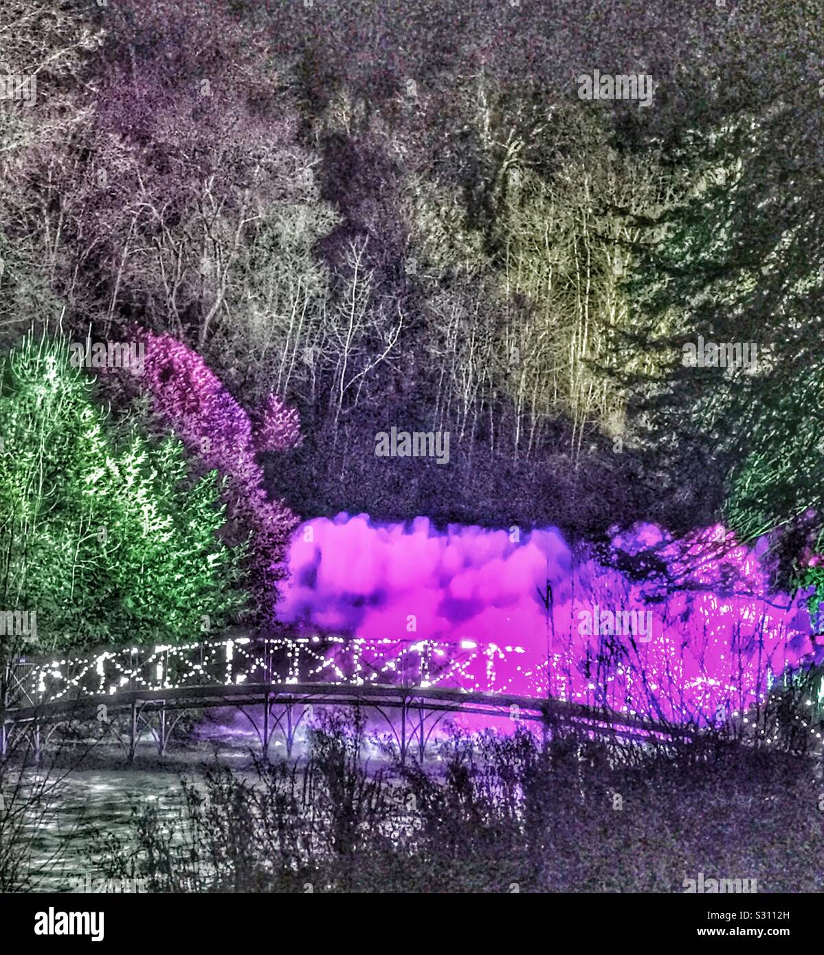 Blenheim Palace Illuminated Christmas Light Trail 2019 - Waterfall with lighting behind, the forest behind and an illuminated bridge with reflections in the water - Smartphone Captured Stock Image