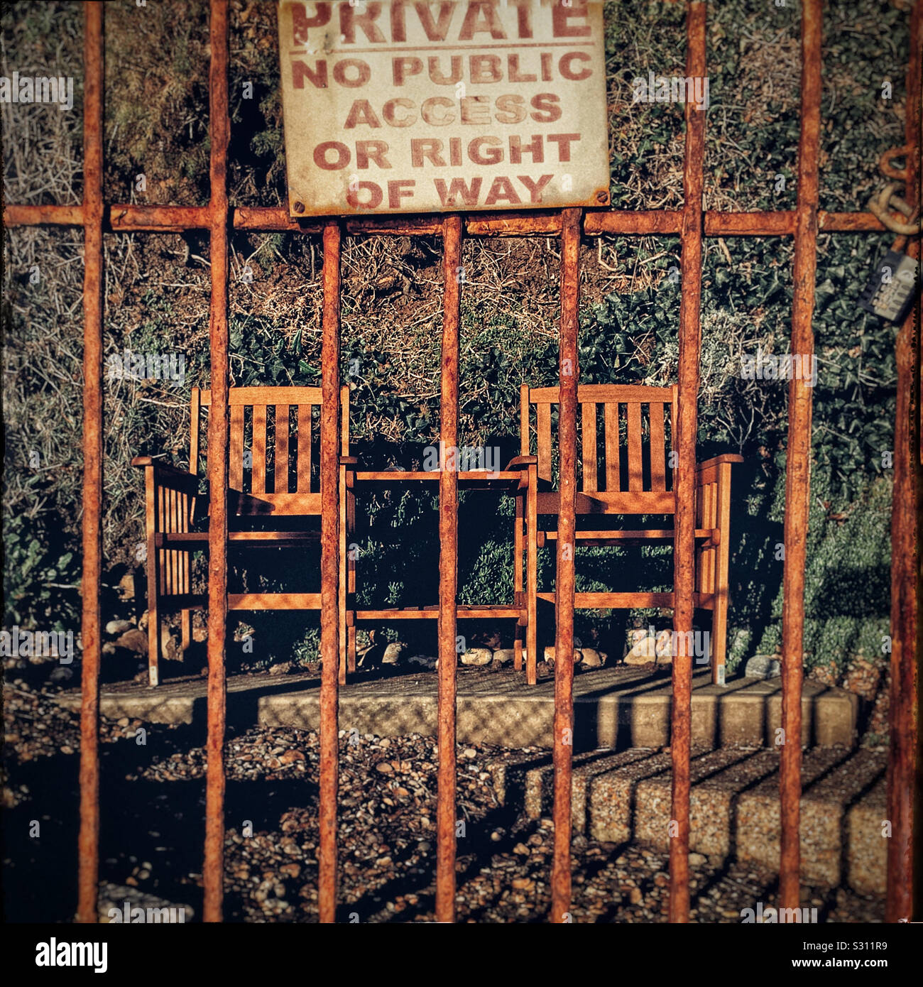 Two wooden chairs behind a rusty gate. - Smartphone Captured Stock Image