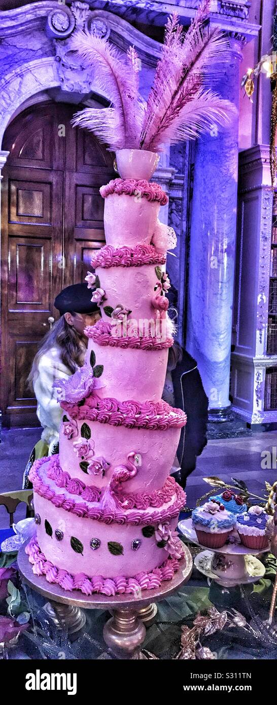 Alice in the Palace At Christmas - Blenheim Palace 2019. Mad Hatters Tea Party Crooked tiered Cake iced in Pink with Flamingos, Roses and Feathers as Decoration. Stock Photo