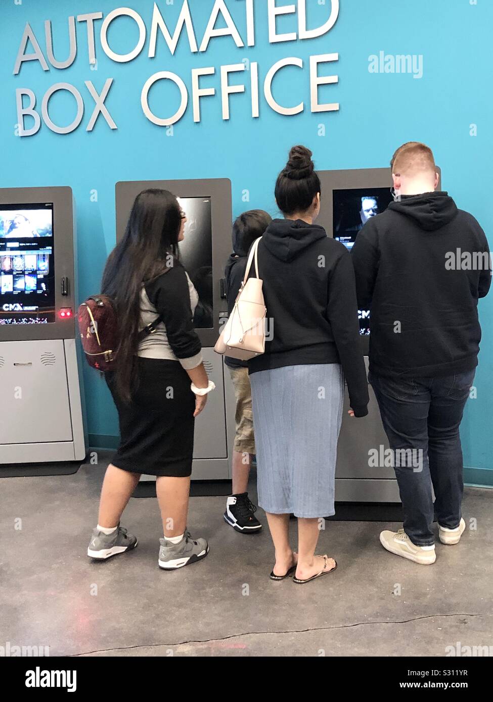 Teenagers buying movie tickets at an automated box office kiosk. - Smartphone Captured Stock Image