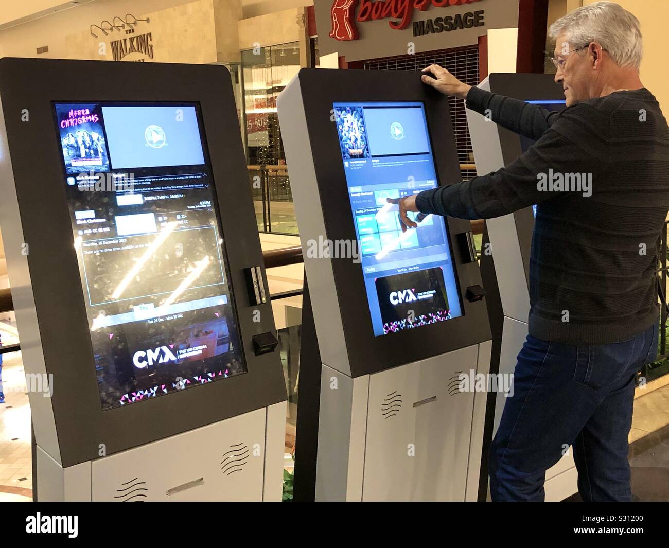 Senior man purchasing a movie ticket at an automated ticket machine in the lobby of a movie theater in a shopping mall. - Smartphone Captured Stock Image