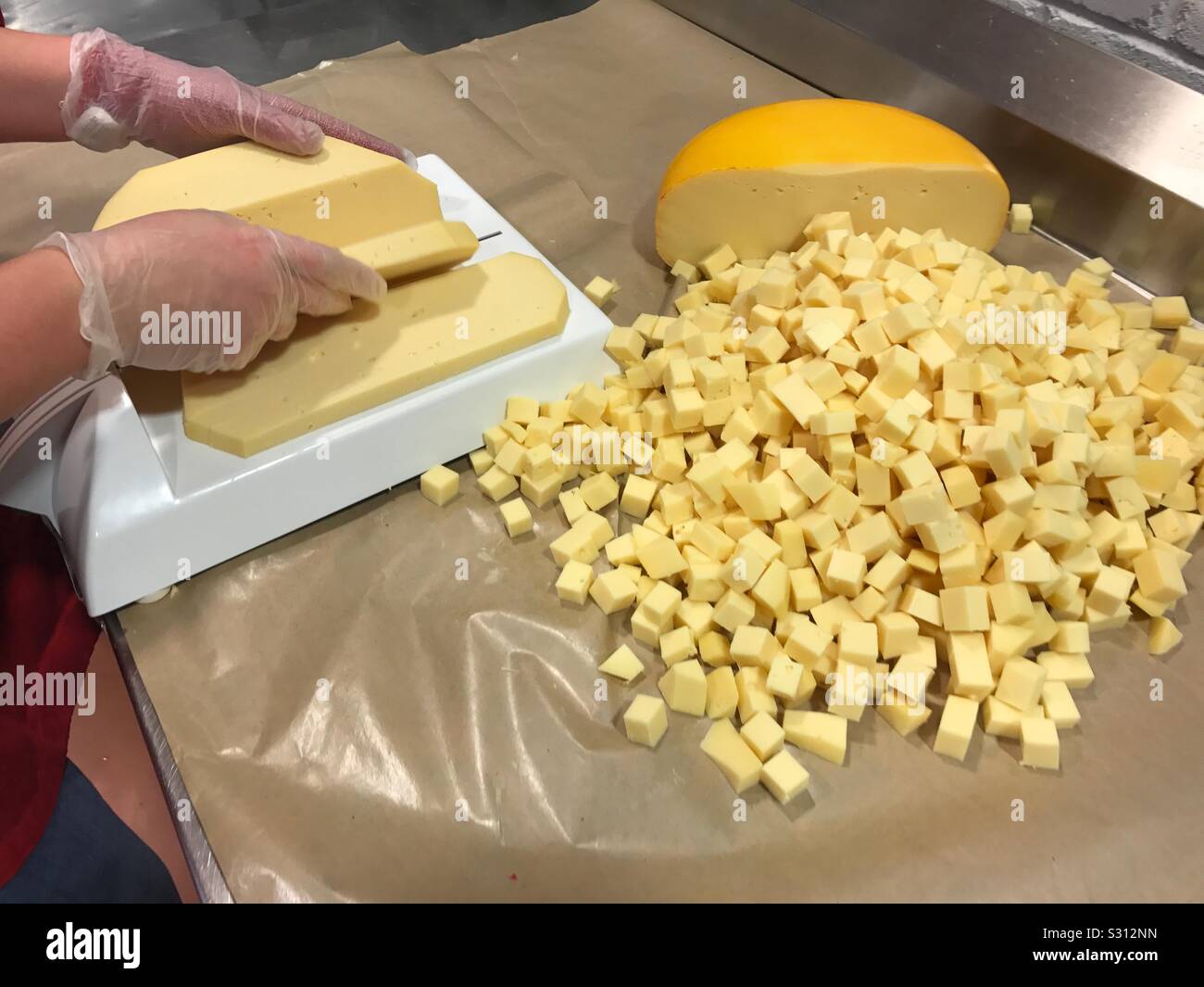 A woman cuts red gouda cheese into cubes. Stock Photo