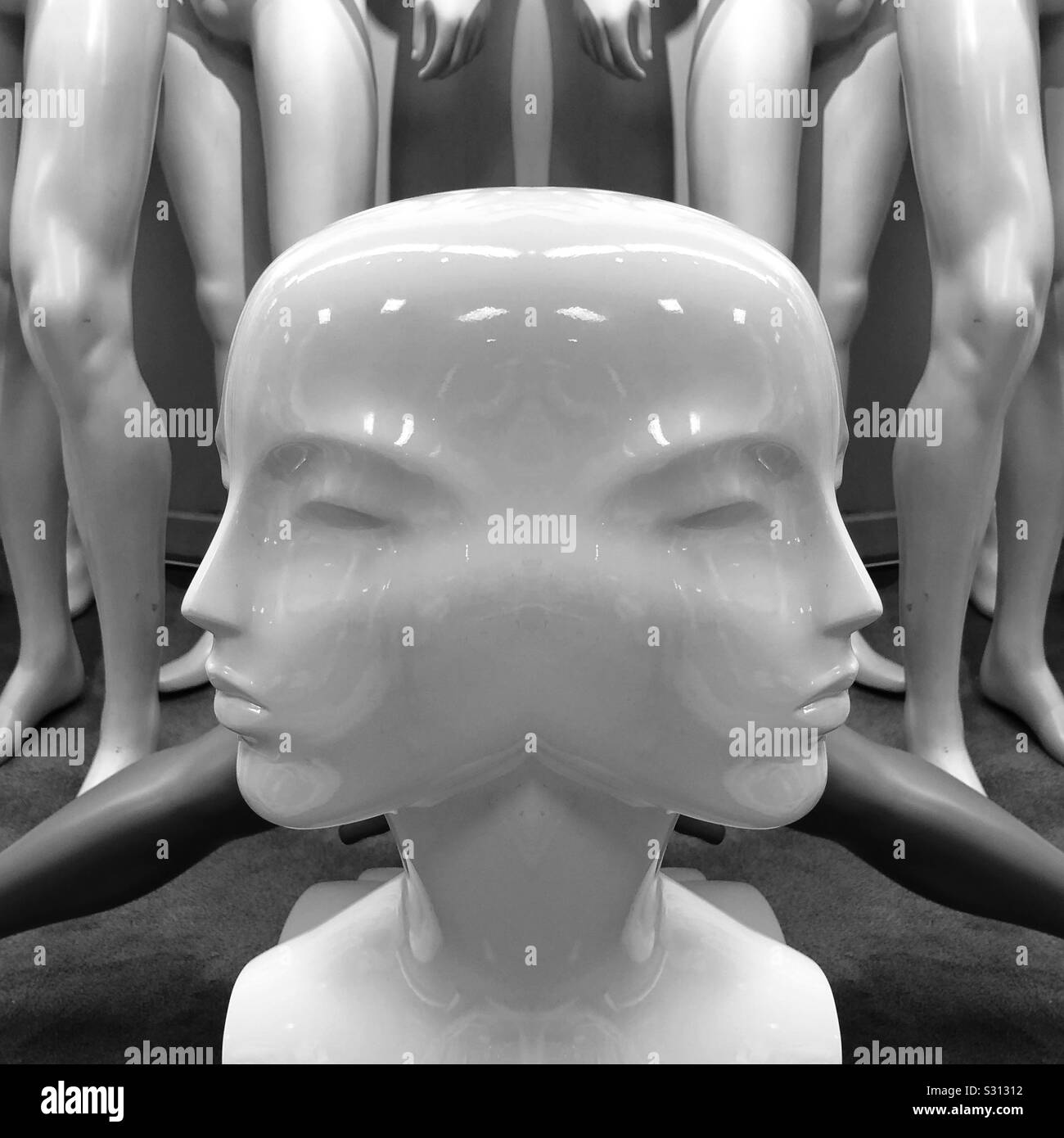 An abstract digital artwork in black and white featuring a two faced mannequin head with mannequin legs in the background Stock Photo