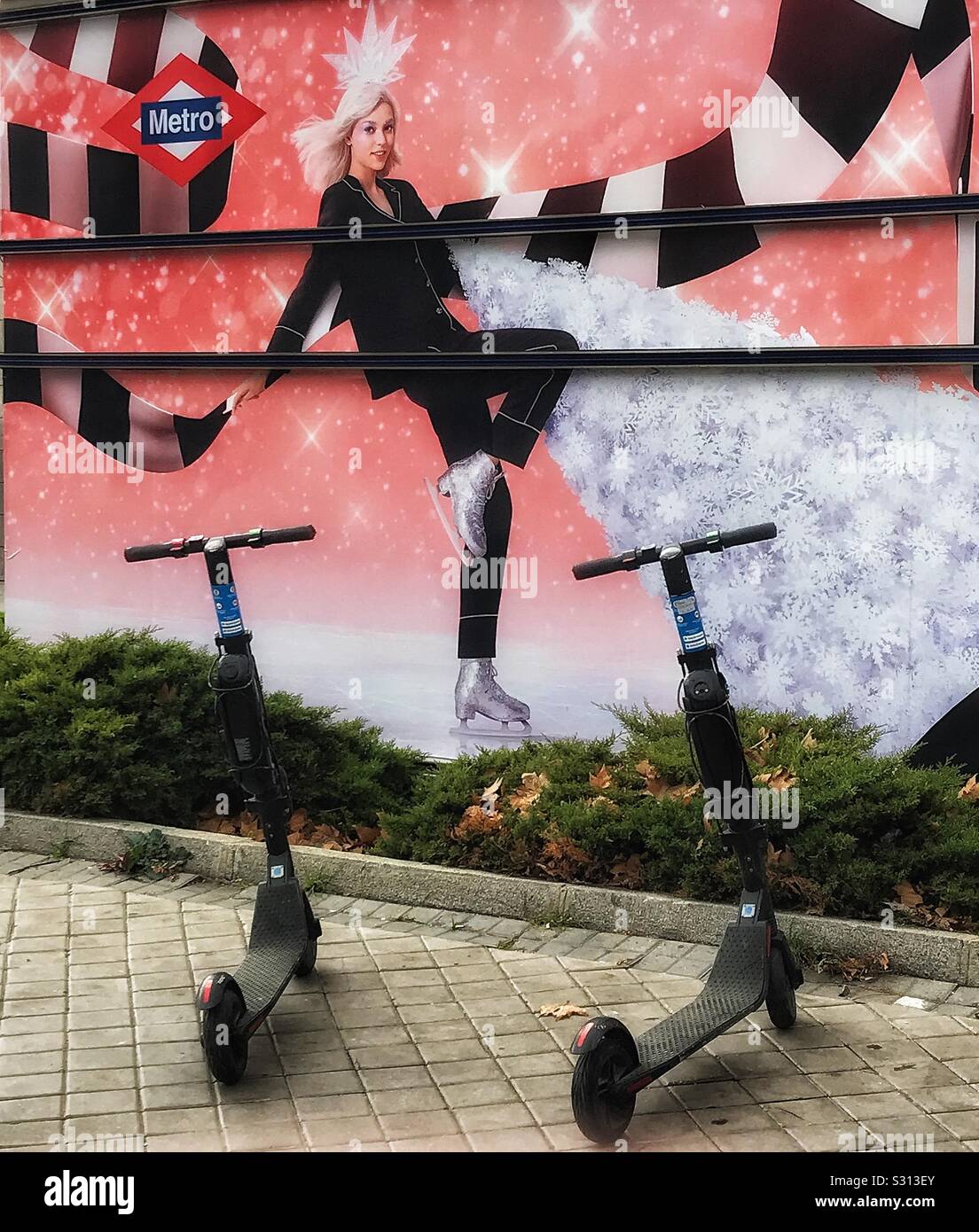 Two electric scooters available for hire parked in the pavement in front of a wall near a metro station, the wall being painted with a mural design Stock Photo