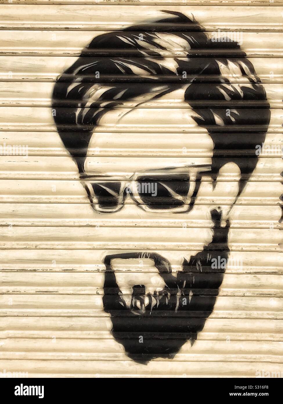 Shutter art. The portrait of a man with a beard and dark glasses is painted in black on the white shutters of a barbershop. Stock Photo