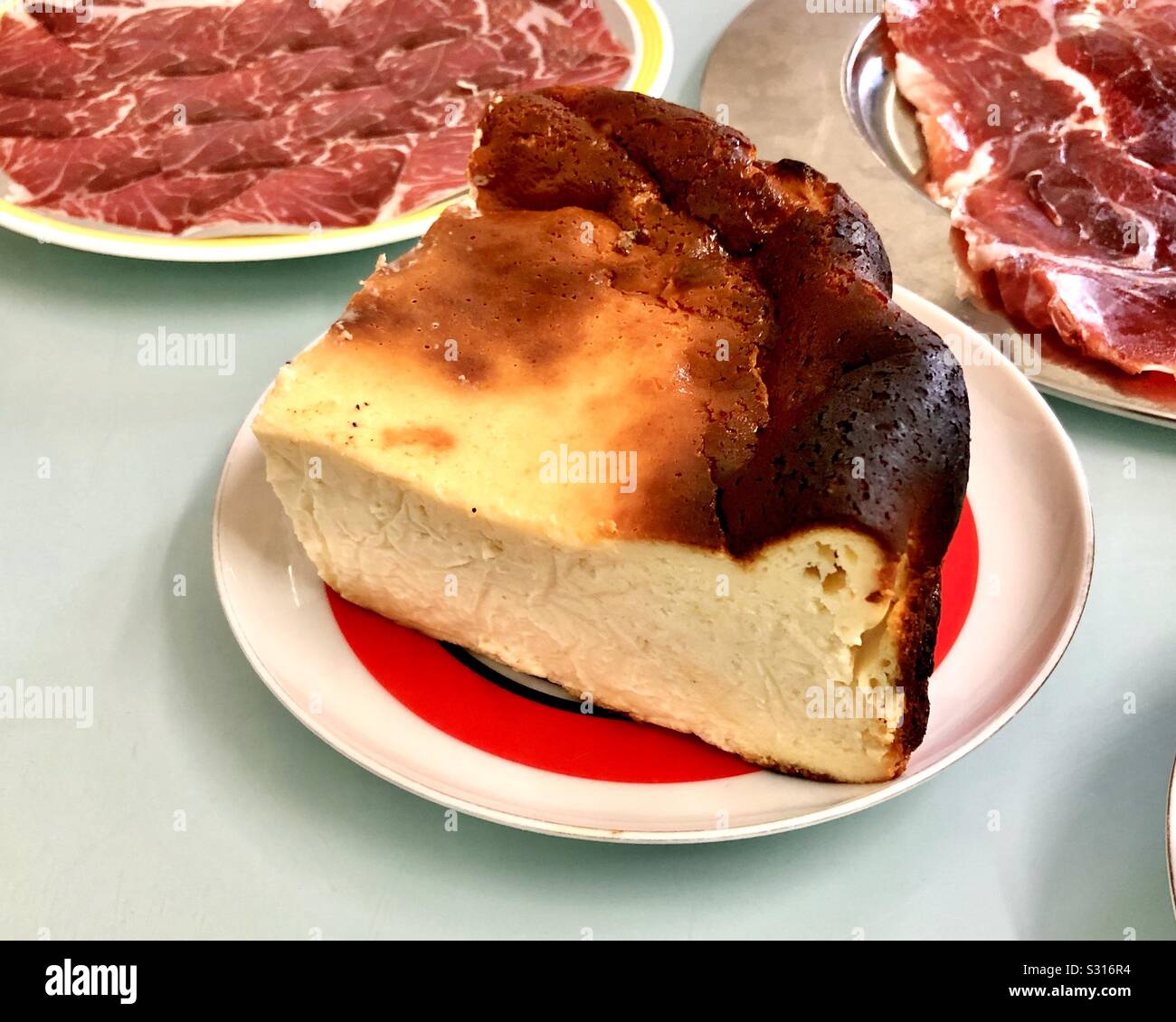 Basque style burnt cheesecake on a plate, with iberico ham plates - Smartphone Captured Stock Image