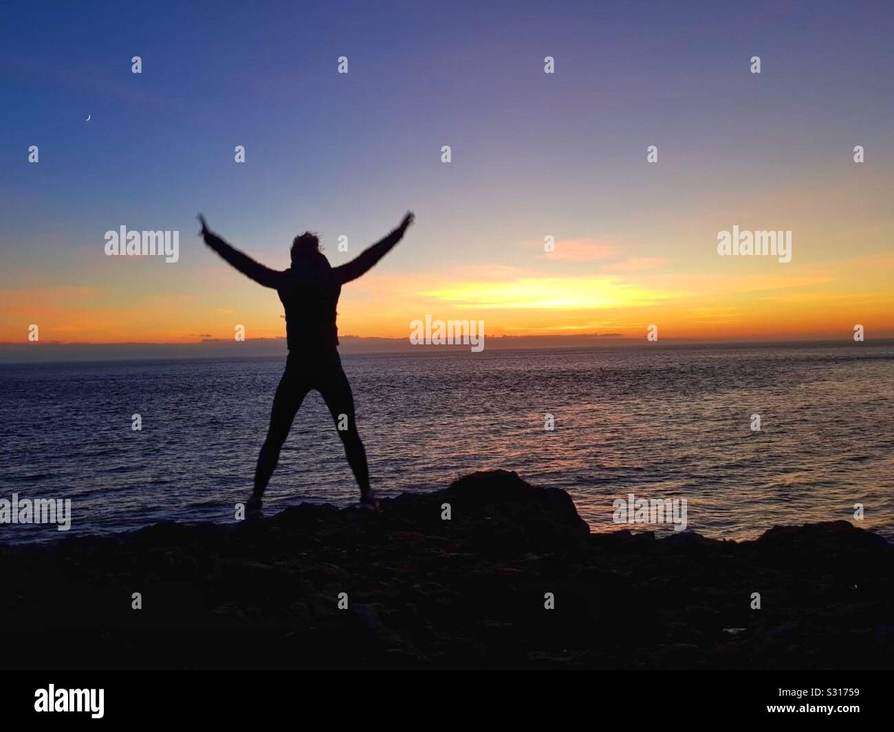 Young woman doing Star Jumps on the coast at sunset. - Smartphone Captured Stock Image