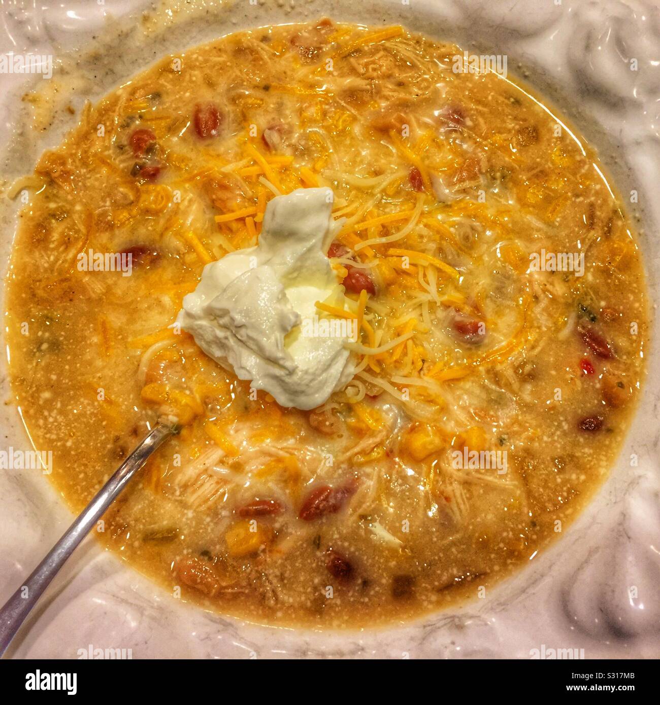 Chicken chili in white bowl with shredded cheese, sour cream and spoon. Stock Photo