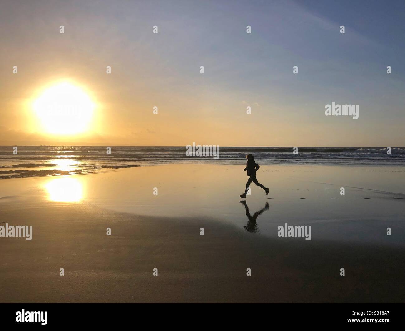 Young woman running across a sandy beach at sunset, South Wales, January. Stock Photo