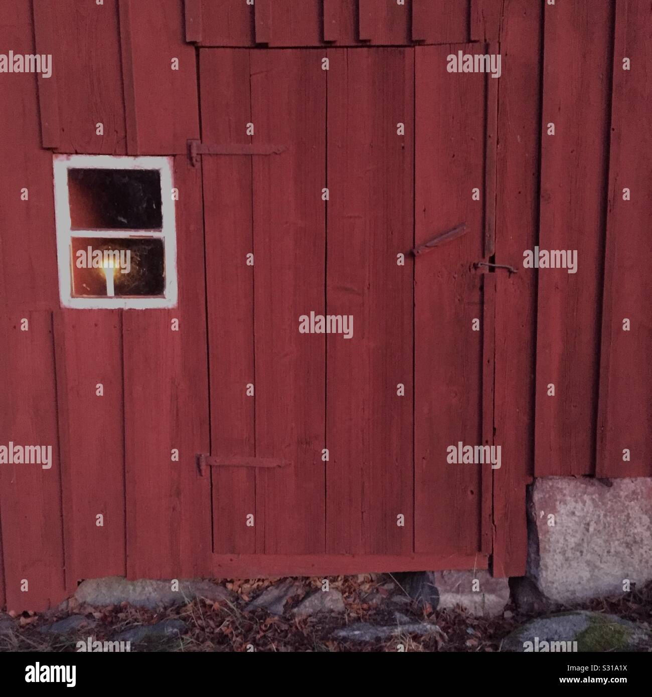 Old red-painted wooden house, Falu color, with closed door and a burning candle in the window. - Smartphone Captured Stock Image