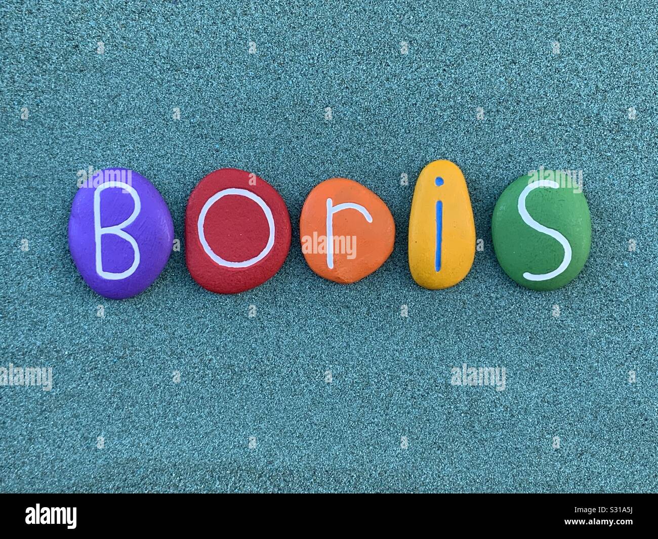 Boris, male given name composed with multi colored stone letters over green sand Stock Photo
