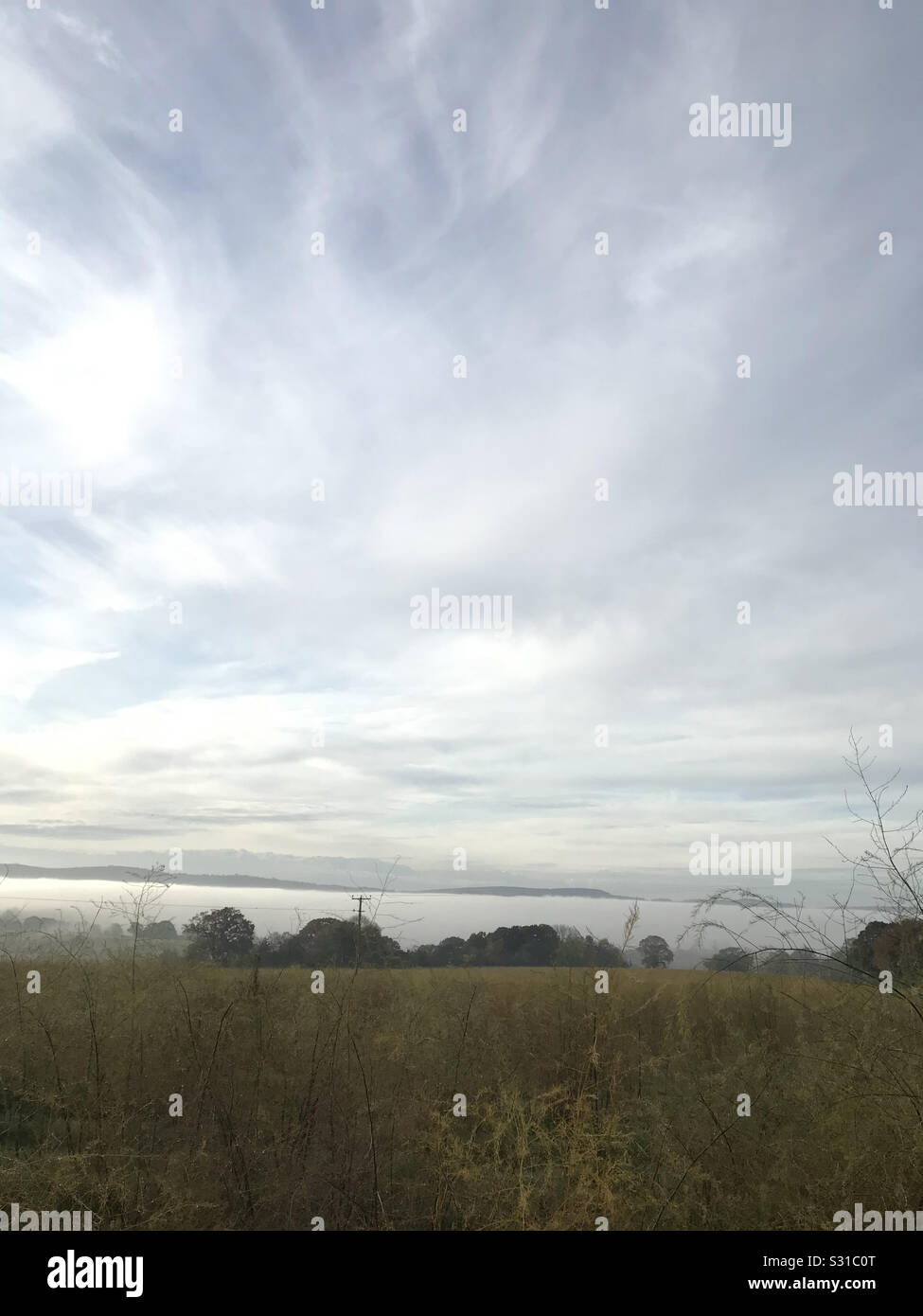 View of misty hills, over fields with dramatic blue sky with clouds - Smartphone Captured Stock Image