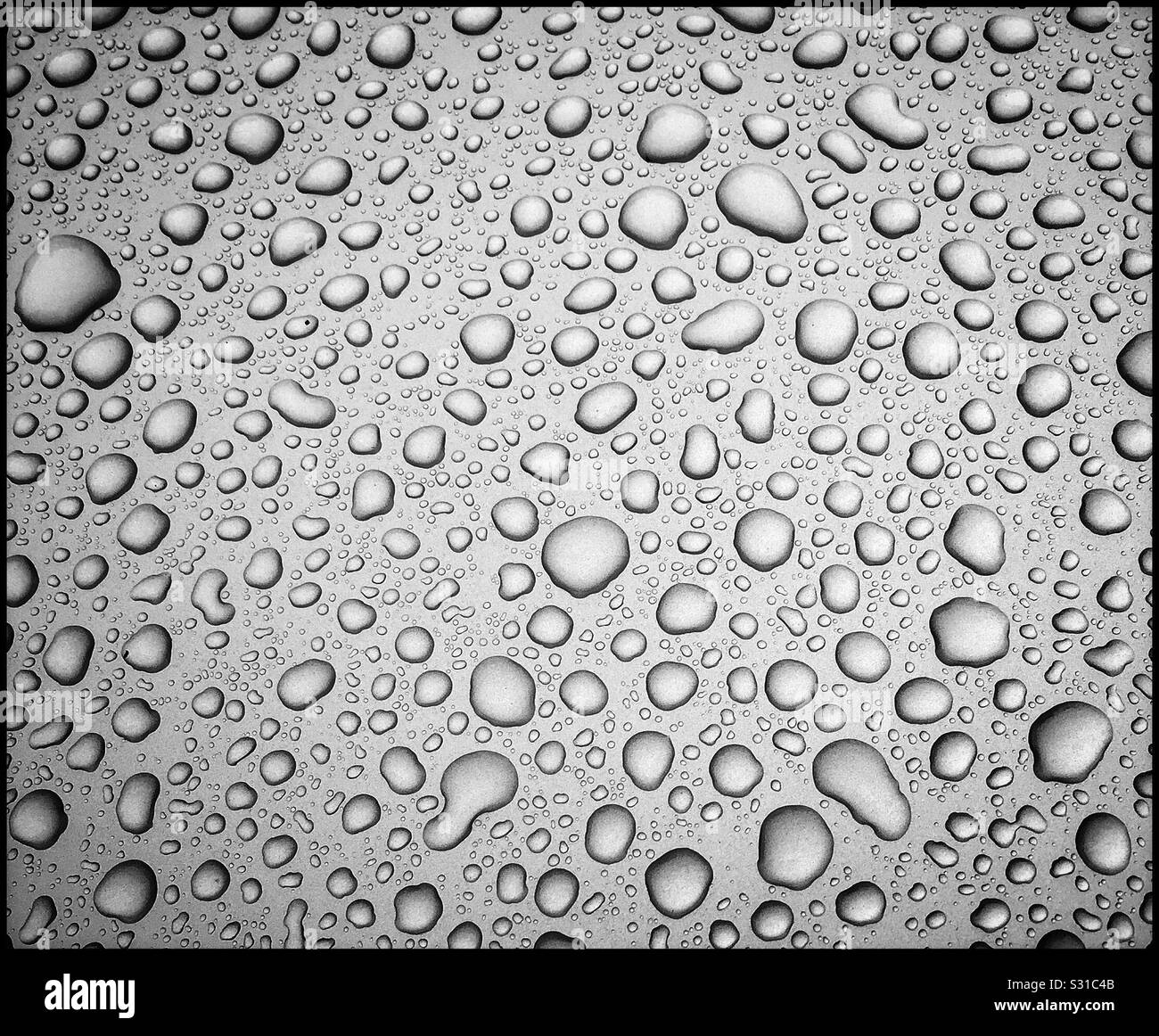 Irregular shaped water droplets on a shiny neutral coloured surface. A graphic image with lots of different shapes & many potential uses? Photo Credit -© COLIN HOSKINS. - Smartphone Captured Stock Image