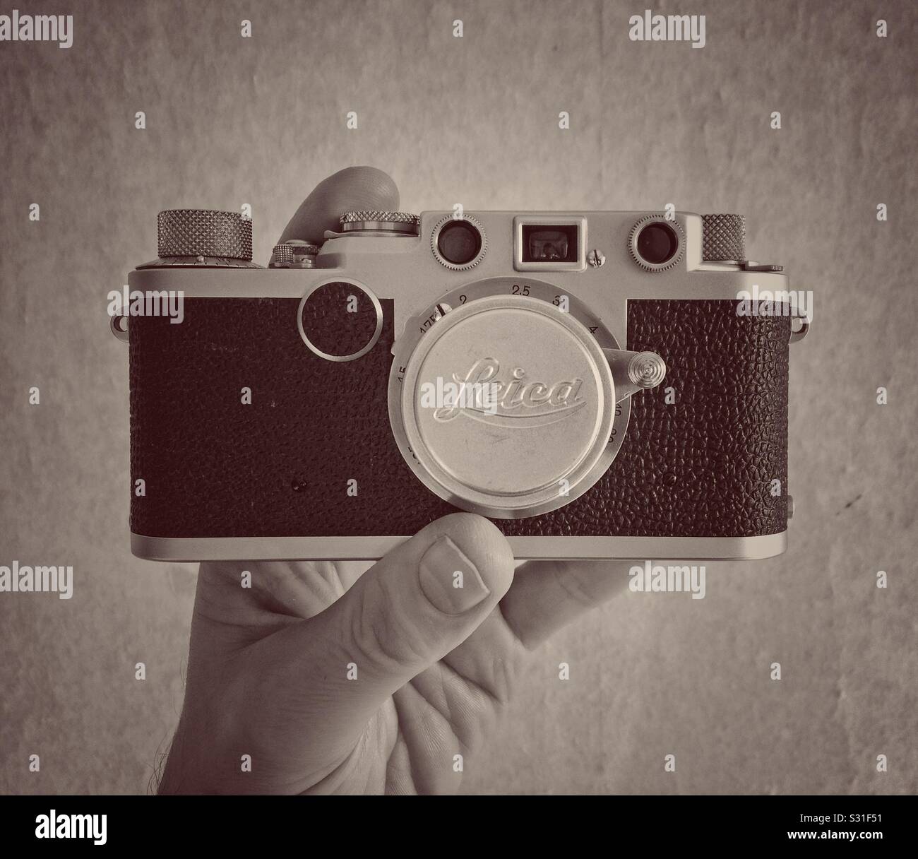 A sepia photograph of man’s hand holding a Leica IIf with a 35 mm f/3.5 Elmar lens - Smartphone Captured Stock Image