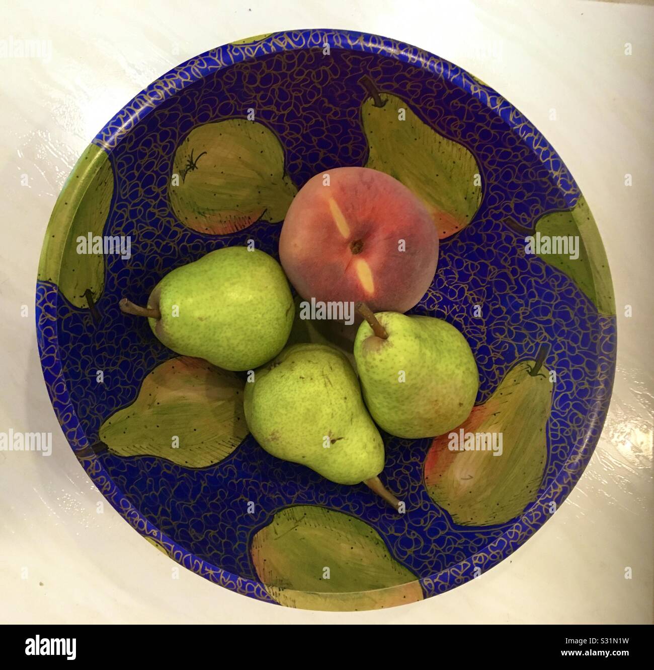 Three pears and one peach on a hand-painted wooden bowl with paintings of peaches on blue. - Smartphone Captured Stock Image