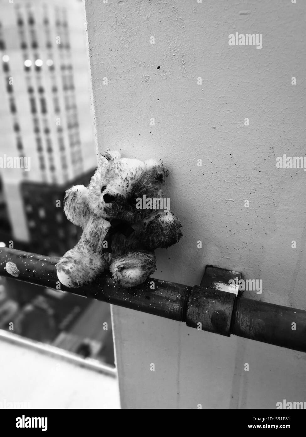 Teddy bear on ledge of highrise building at dusk depicting person contemplating giving up their life by suicide Stock Photo