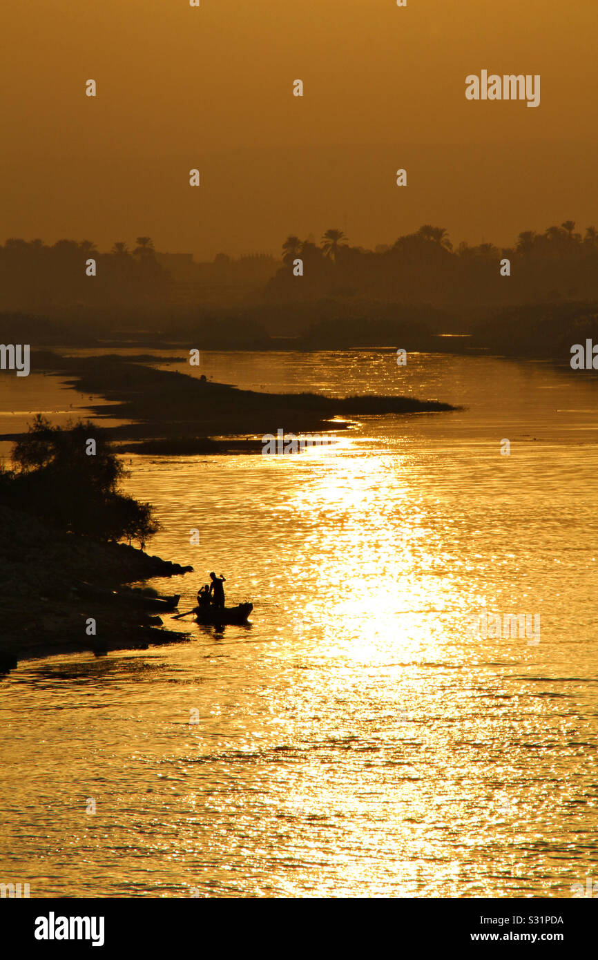 A pair of fishermen in a boat silhouetted by the setting sun on the Nile River in Egypt. Stock Photo