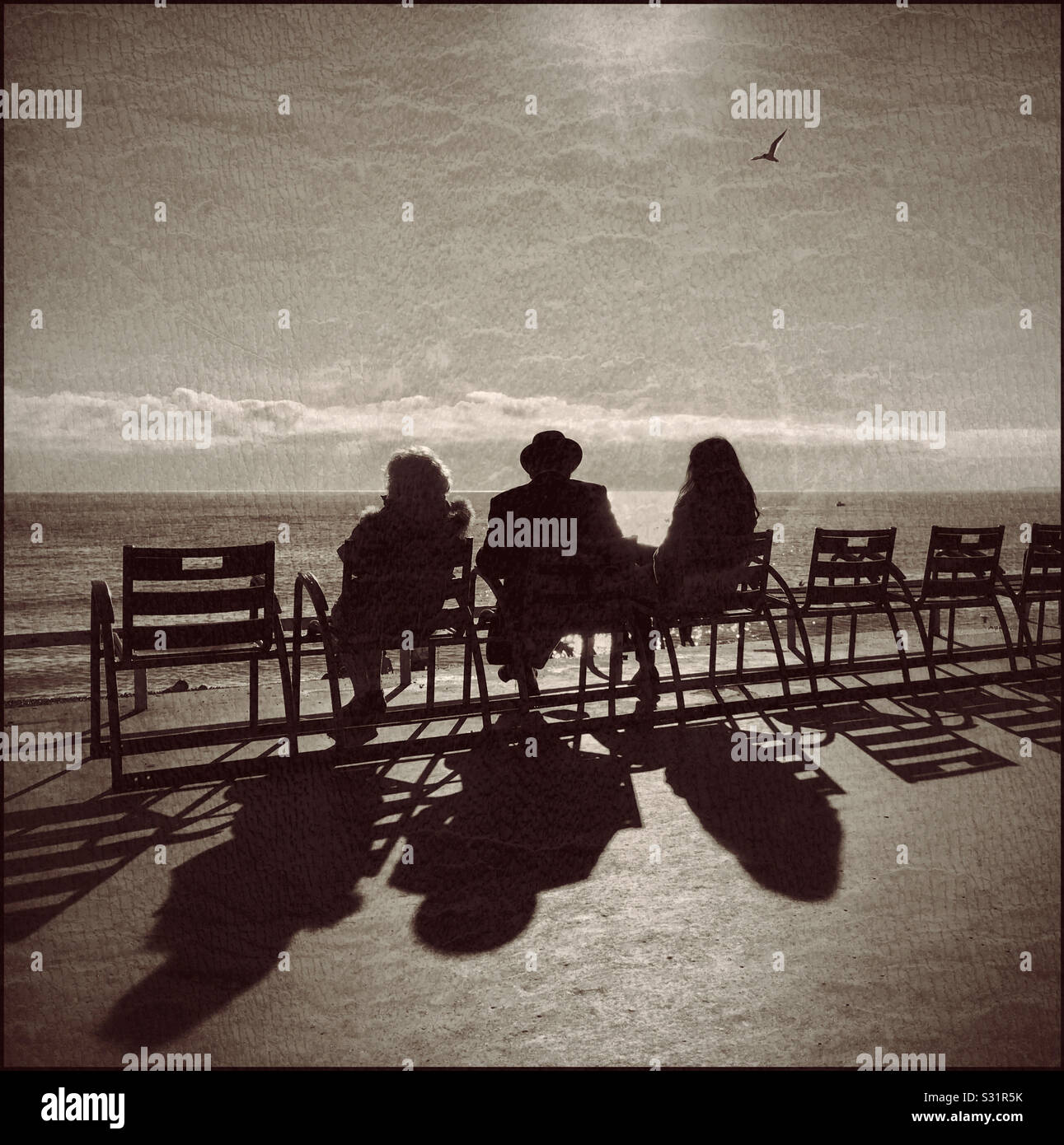 People watch the world go by as they sit on chairs overlooking the Mediterranean Sea during a winter’s afternoon. You can’t beat interesting shadows! Photo Credit © COLIN HOSKINS. - Smartphone Captured Stock Image