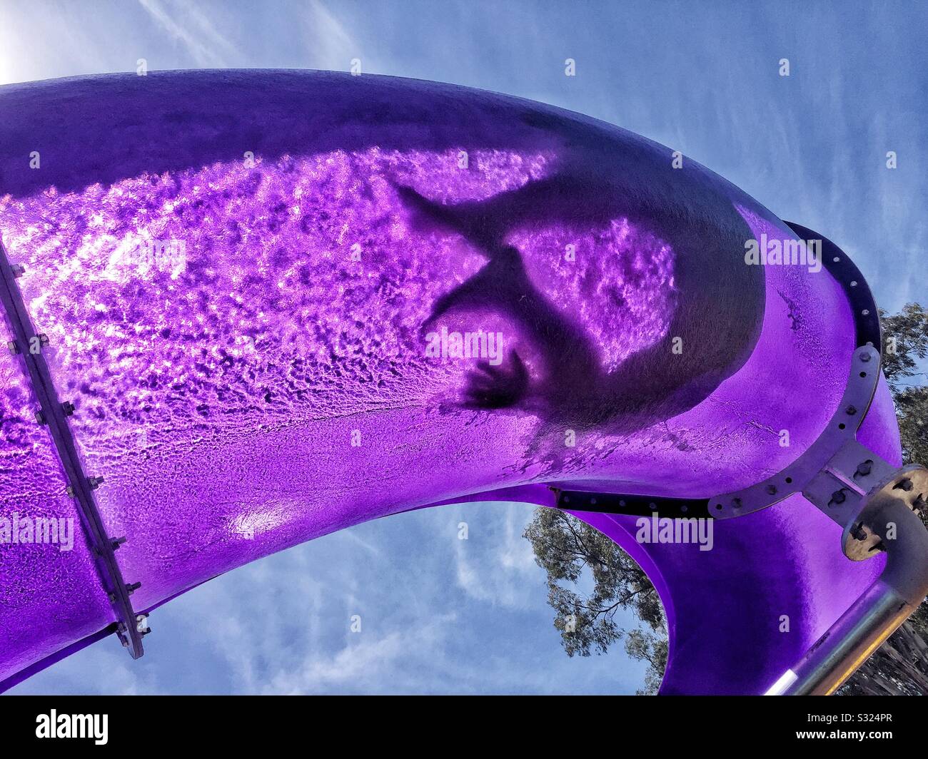 Summer vacation fun, silhouette of adult sliding down purple water slide. Stock Photo