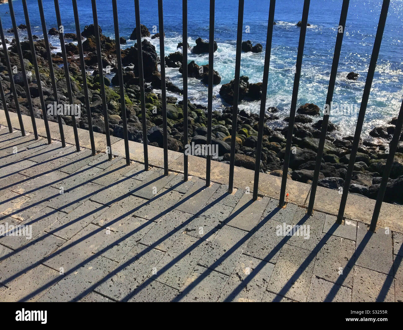 Railings by the sea throw shadows on the footpath Playa San Juan, Tenerife - Smartphone Captured Stock Image